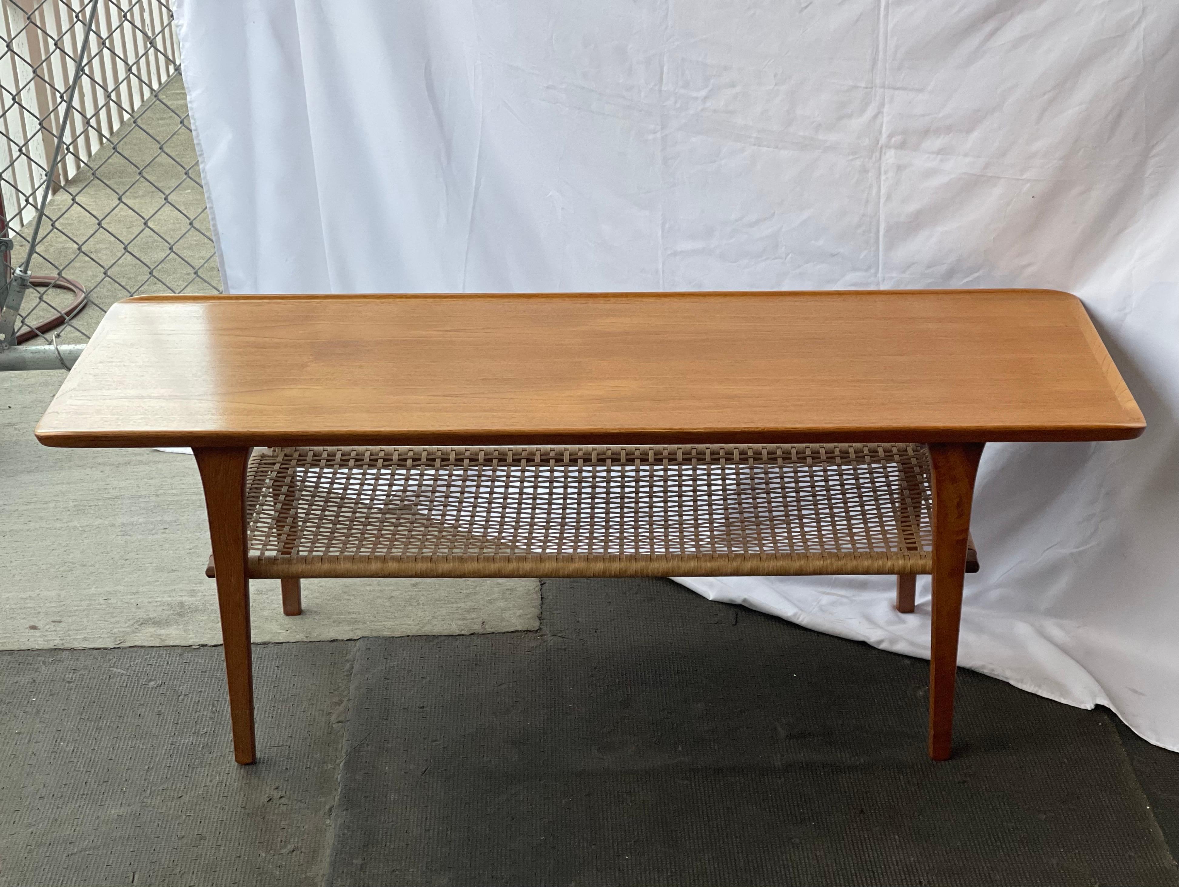 A beautiful solid teak mid century modern coffee table with rattan shelf. A classic design and perfect addition to any space.