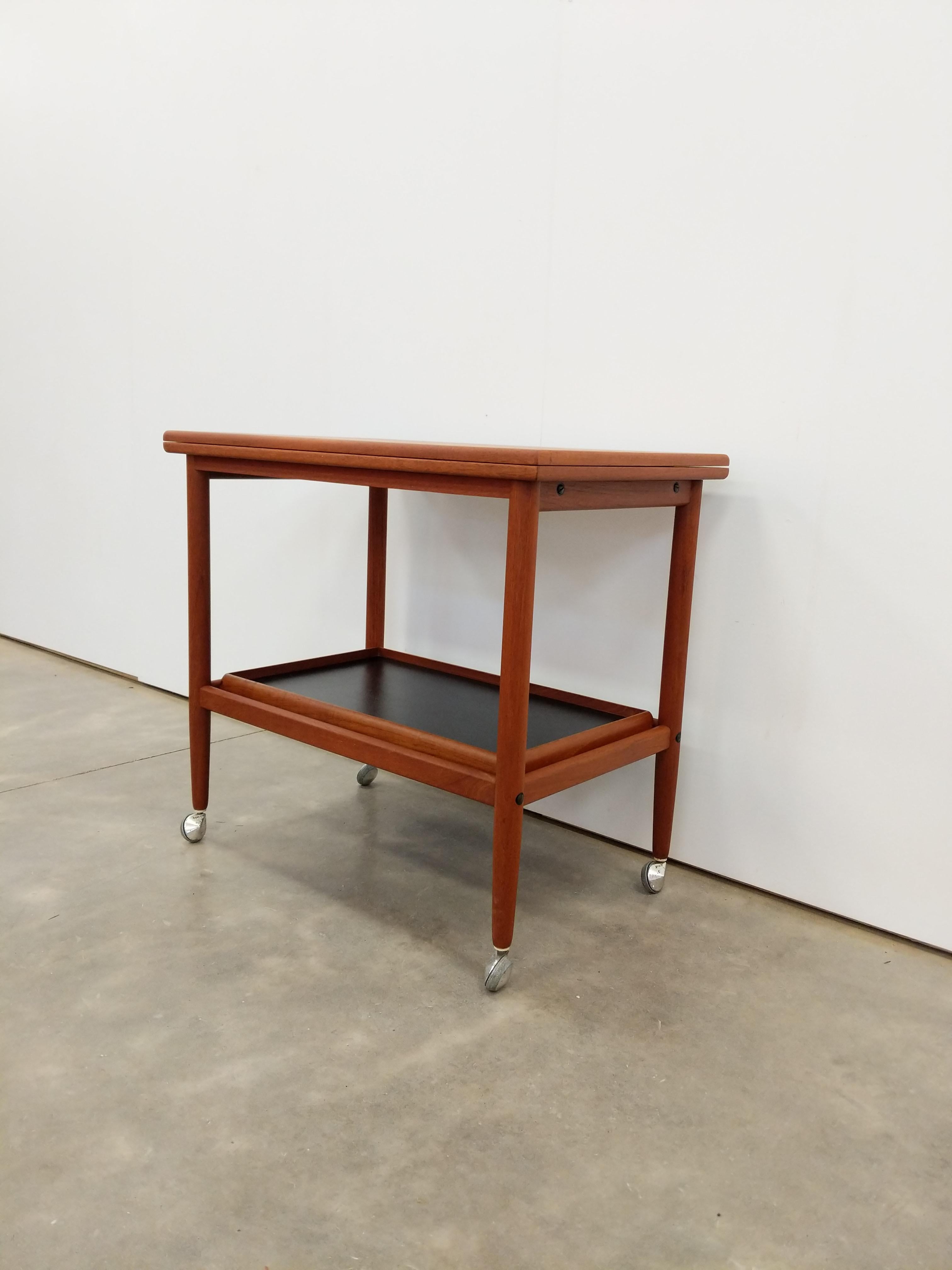 Autentico carrello vintage danese / moderno scandinavo in teak, tavolo / carrello / tavolino su ruote.

Meccanismo di espansione e vassoio rimovibile che si adatta al ripiano inferiore (vedi foto).

Marchio 