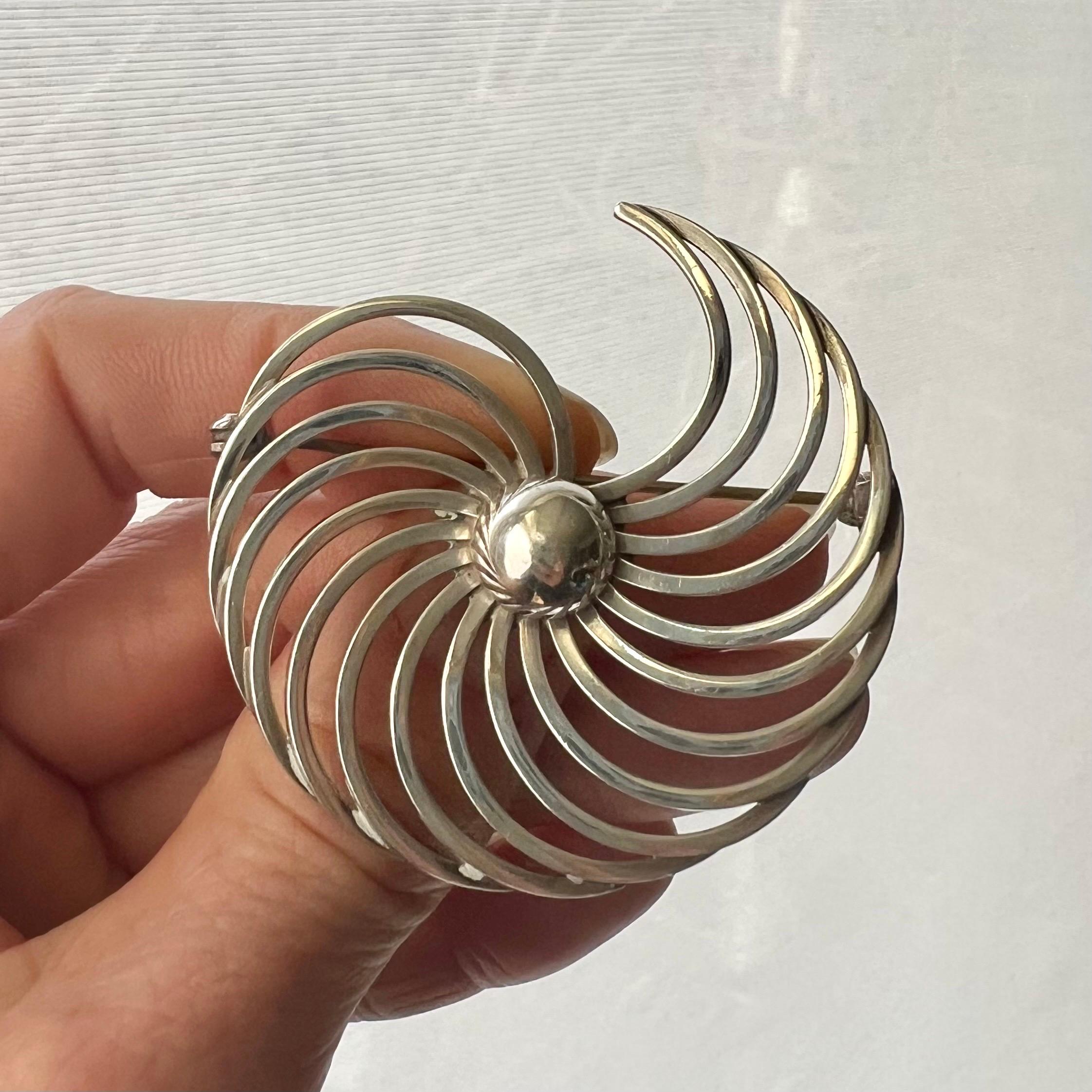 This vintage 1960's sterling silver brooch is created in a swirl design. The brooch is crafted in sterling silver and has a typical 1960's and 1970's modernist design. The center of the brooch is set with a knot. The fabulous design gives movement