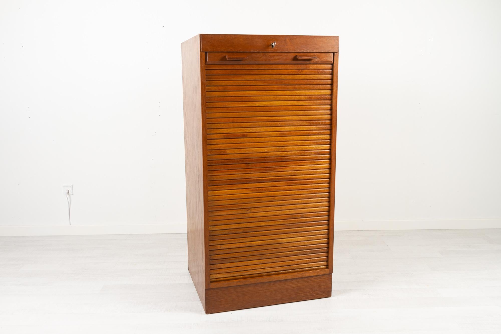 Vintage Danish stained oak cabinet with tambour front, 1960s
Danish modern filing cabinet with vertical sliding tambour door in teak. 10 wide drawers, most with room dividers which can be removed. Rolling door opens with key. Key is included.
Very