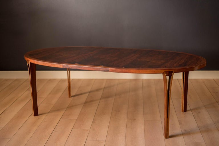 Mid-Century Modern oval shaped extension dining table manufactured by Heltborg Møbler, circa 1970's. Features a stunning display of rich rosewood grains supported by sculptural inset legs with brass details. The table expands with one leaf and can