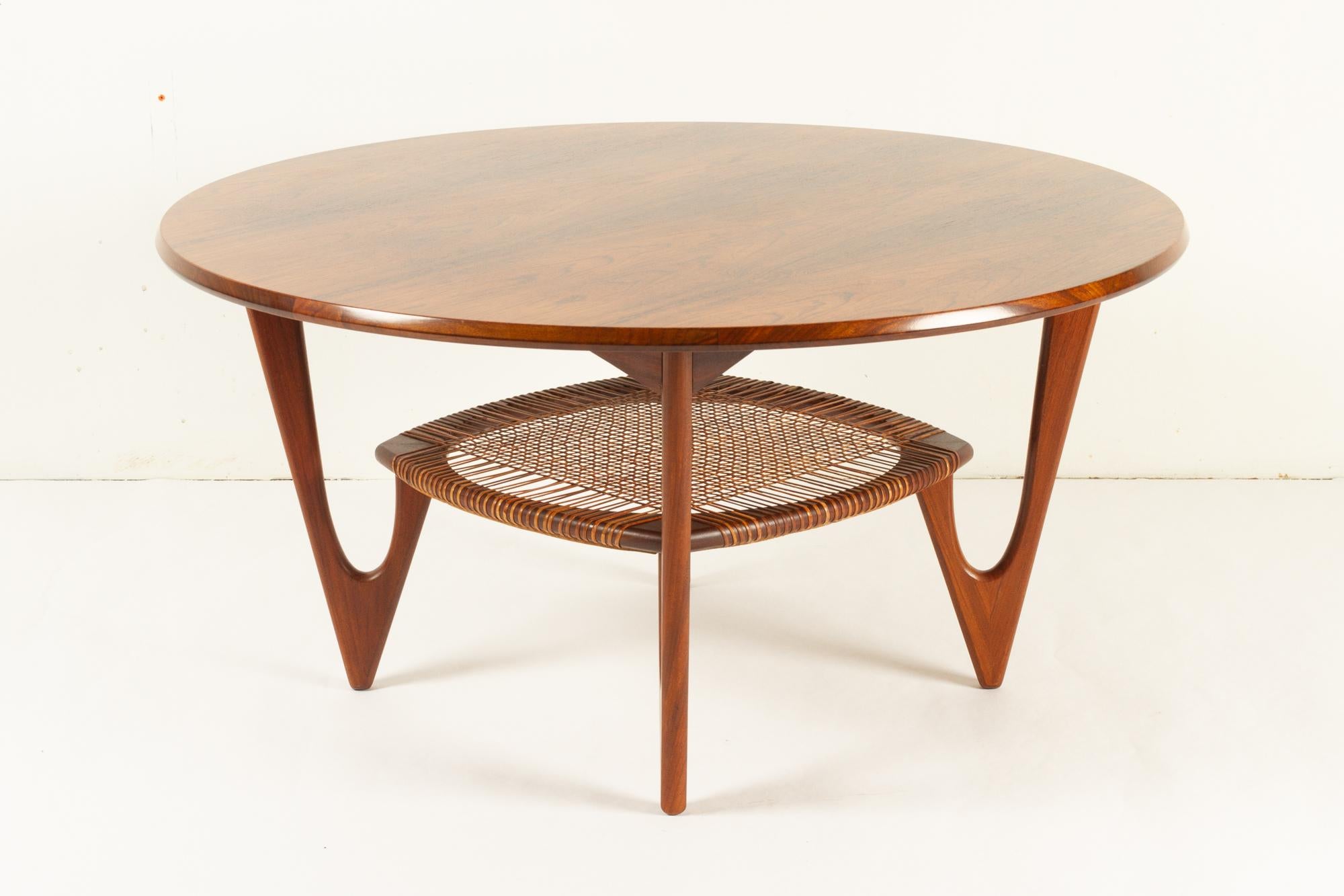 Vintage Danish rosewood coffee table by Kurt Østervig for Jason Møbler, 1950s.
Rare and elegant Mid-Century Modern round coffee table with cane shelf. Sculpted V-shaped legs in dark solid teak. Designed by renowned Danish architect Kurt Østervig in