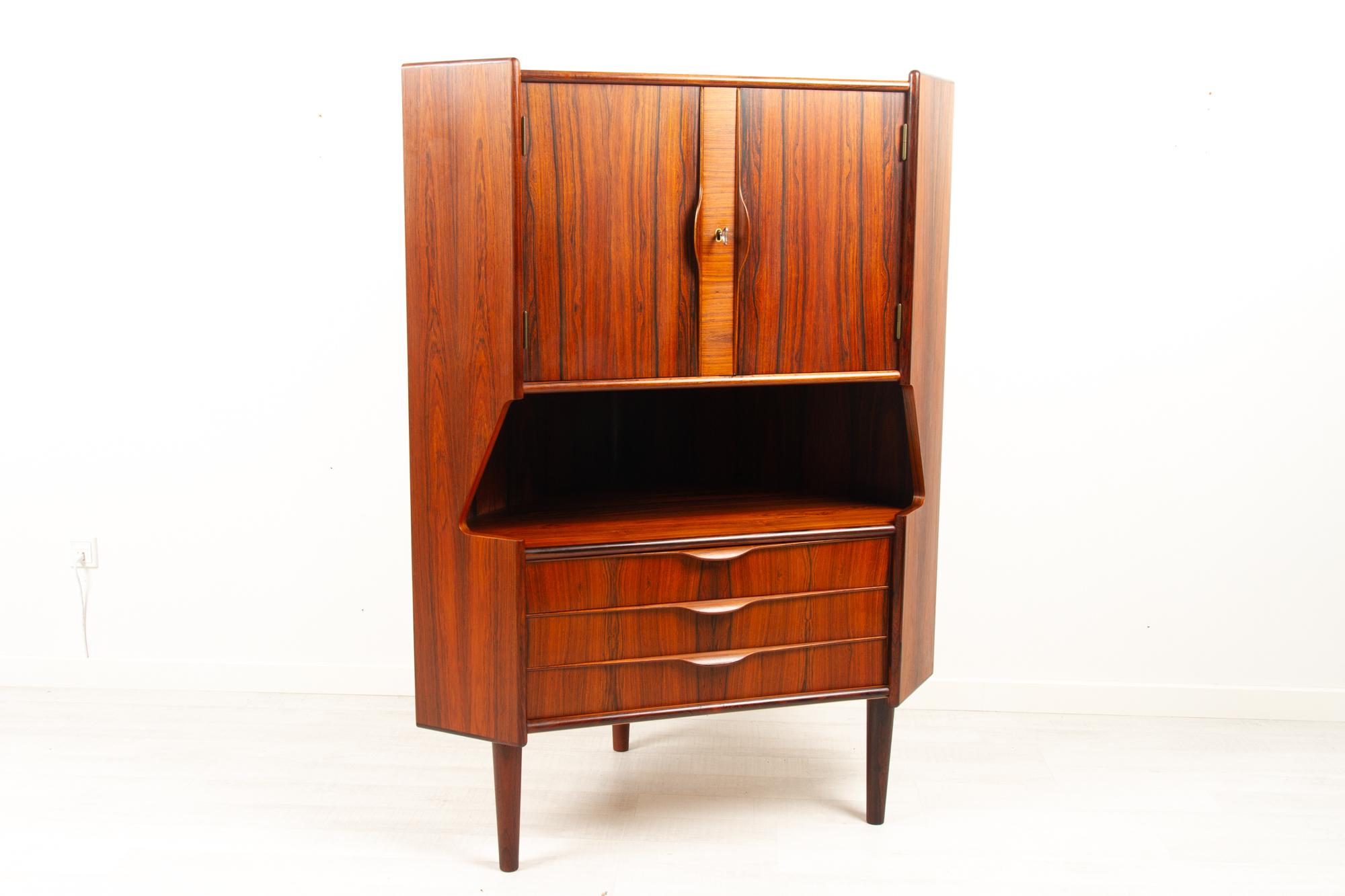Vintage Danish rosewood corner cabinet with dry bar, 1960s
Danish Mid-Century Modern corner cabinet with bar unit and drawers. Cabinet behind double doors with lock and key. Inside decorated mirror and curved shelf. Amble space for glasses and