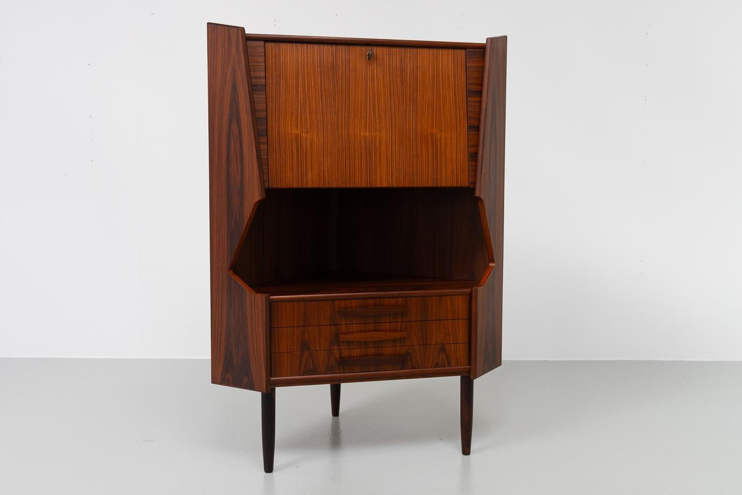 Vintage Danish rosewood corner cabinet with dry bar, 1960s.

Scandinavian Mid-Century Modern corner cabinet with bar unit and drawers. Drinks cabinet behind drop down door with lock and key. Inside is decorated mirror and curved shelf. Amble space
