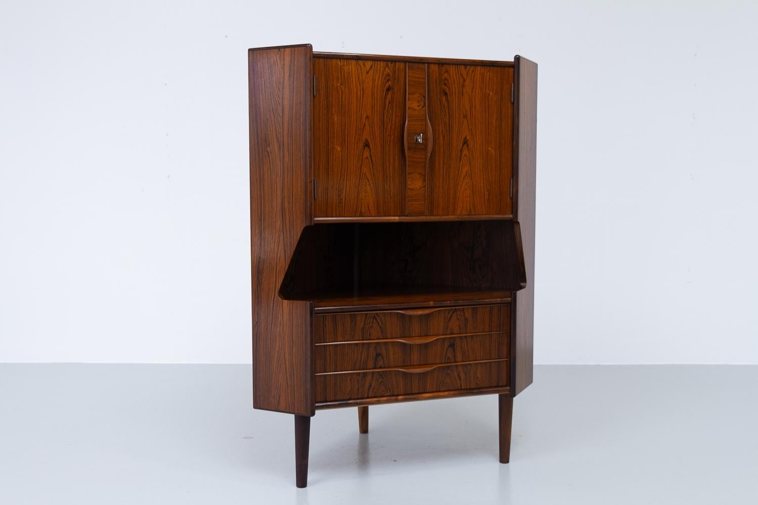 Vintage Danish rosewood corner cabinet with dry bar, 1960s.

Scandinavian Mid-Century Modern corner cabinet with bar unit and drawers. Drinks cabinet behind double doors with lock and key. Inside is decorated mirror and curved shelf. Amble space for