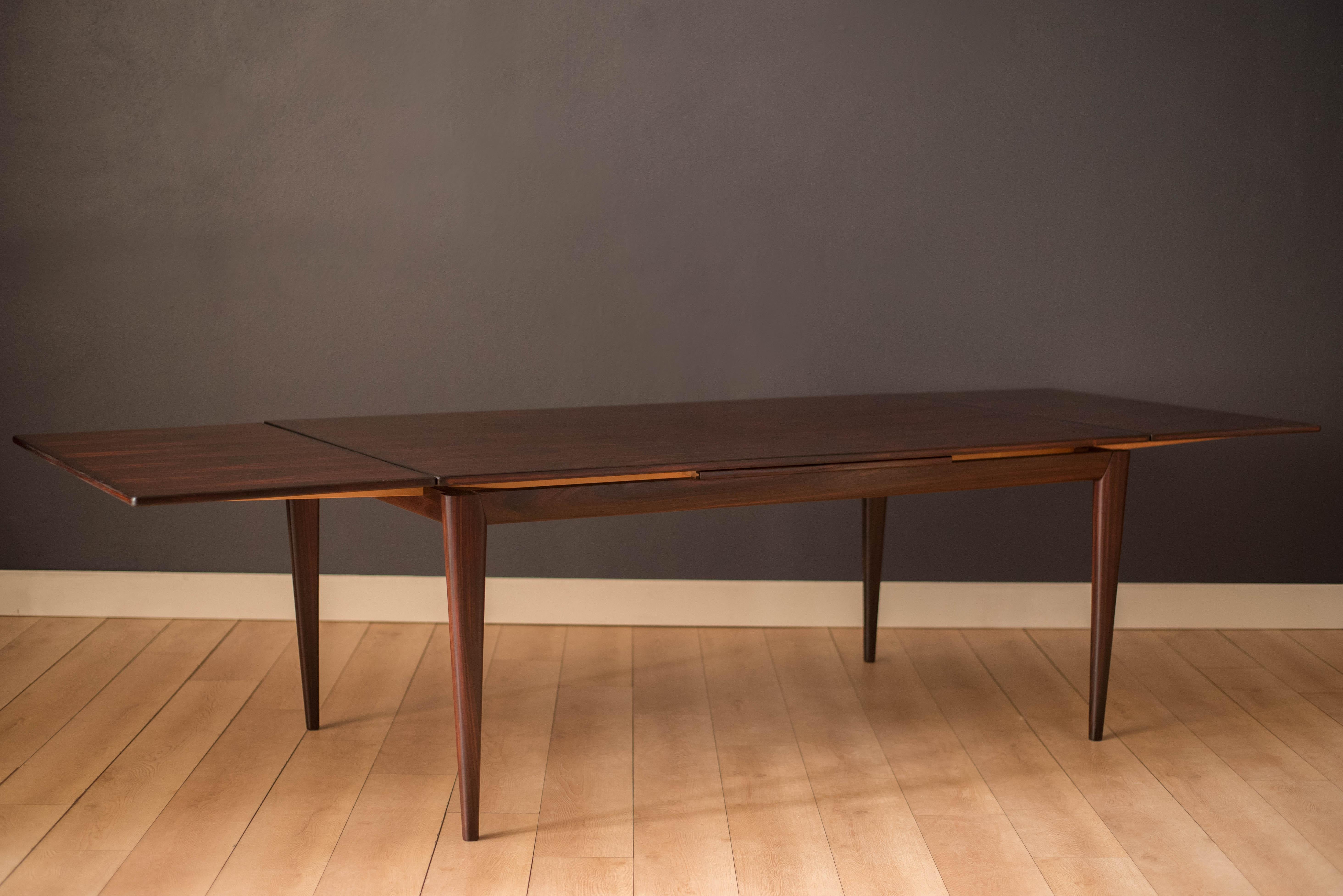 Mid-Century Modern extension dining table designed by Niels Otto Møller for J.L. Møllers Møbelfabrik, Denmark. Features a stunning display of rich rosewood grains supported by thick tapered legs. This piece offers two draw leaf extensions that