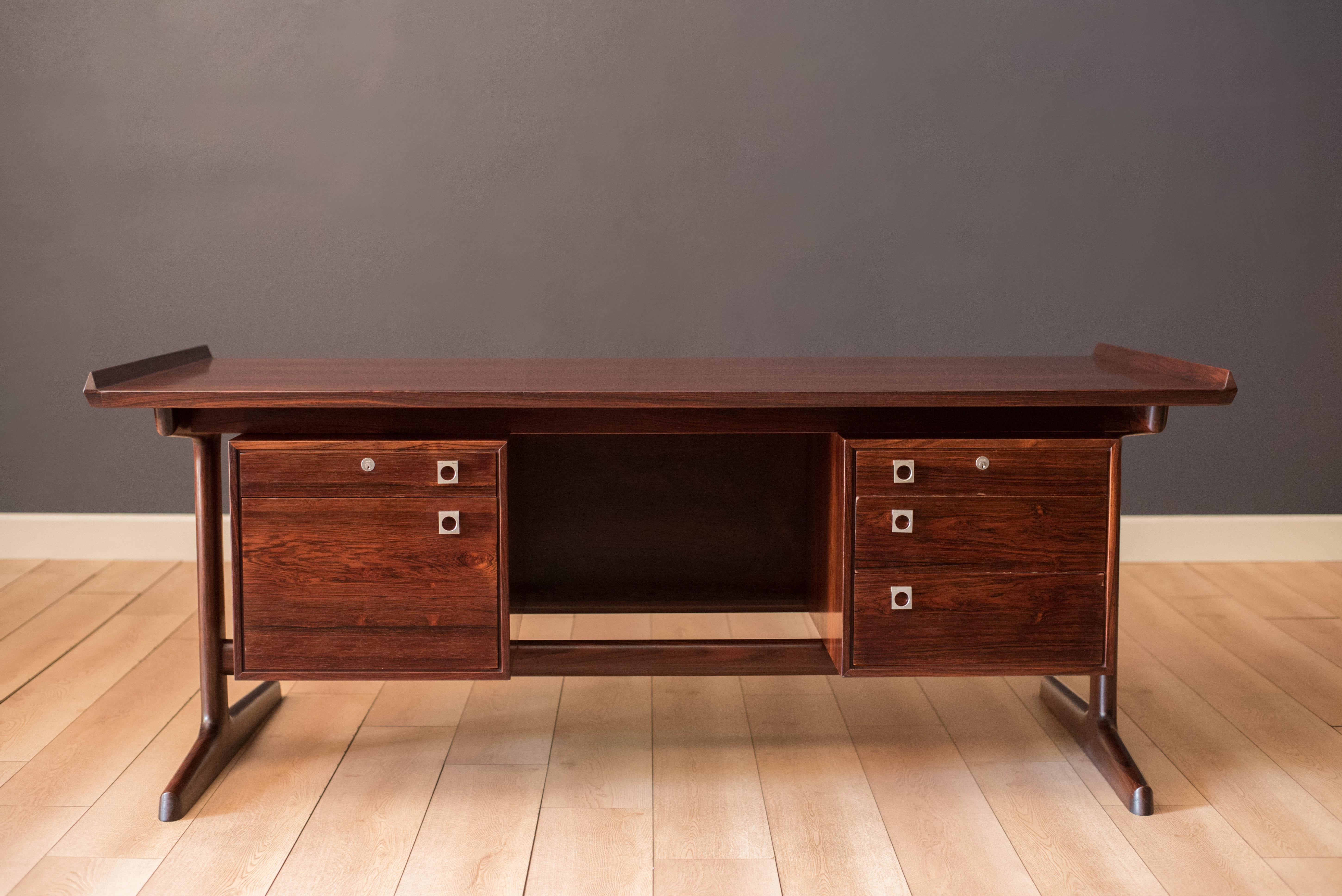 Mid-Century Modern executive desk in rosewood by H.P. Hansen, Denmark circa 1960s. Features a floating top with raised lip edges and a unique external supporting leg base. This piece offers plenty of storage equipped with five dovetailed drawers