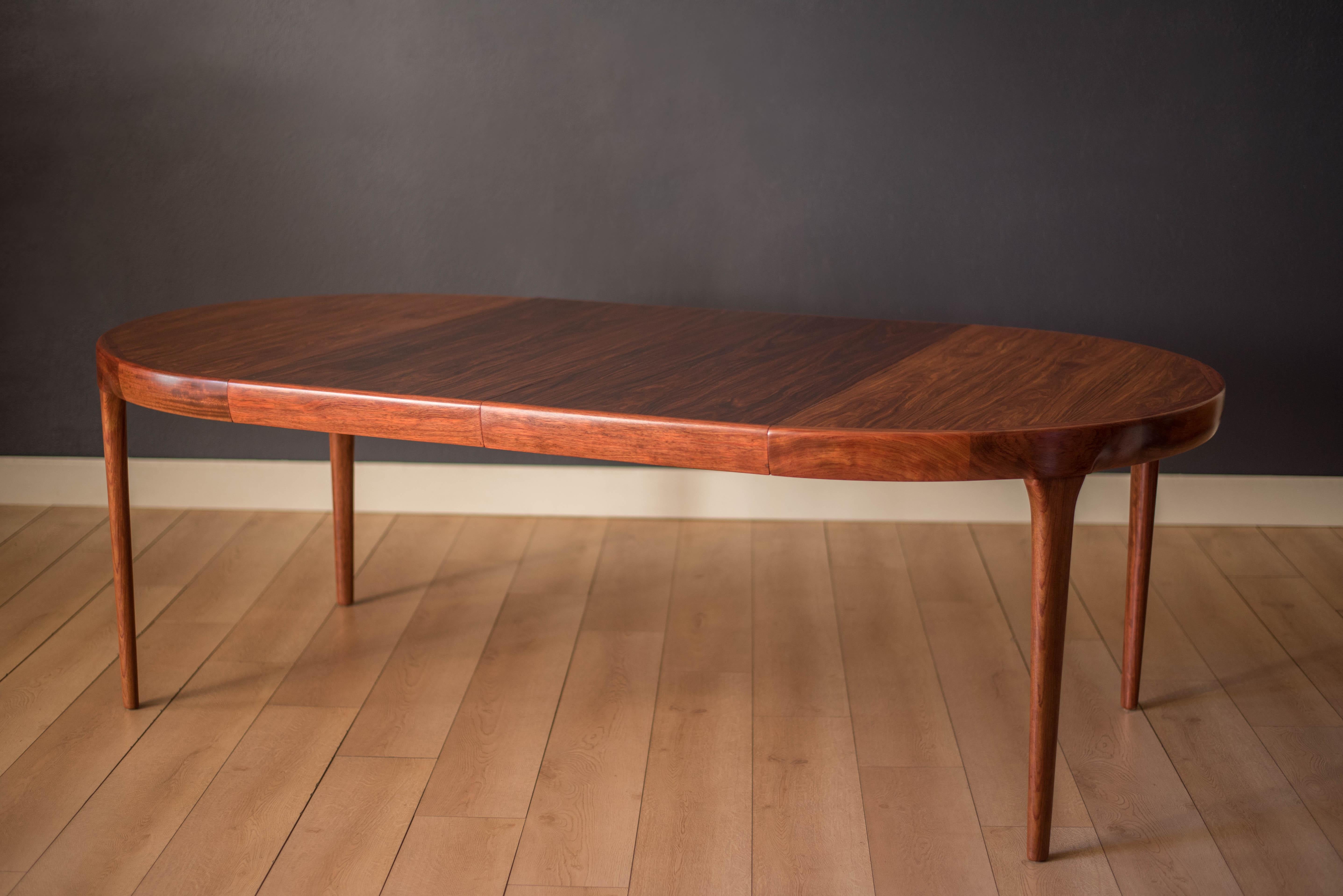 Mid-Century Modern dining table designed by Ib Kofod-Larsen for Faarup Møbelfabrik. This piece displays continuous Brazilian rosewood grains with solid edge banding and a seamless sculpted apron. The table extends with two leaves that can fit up to
