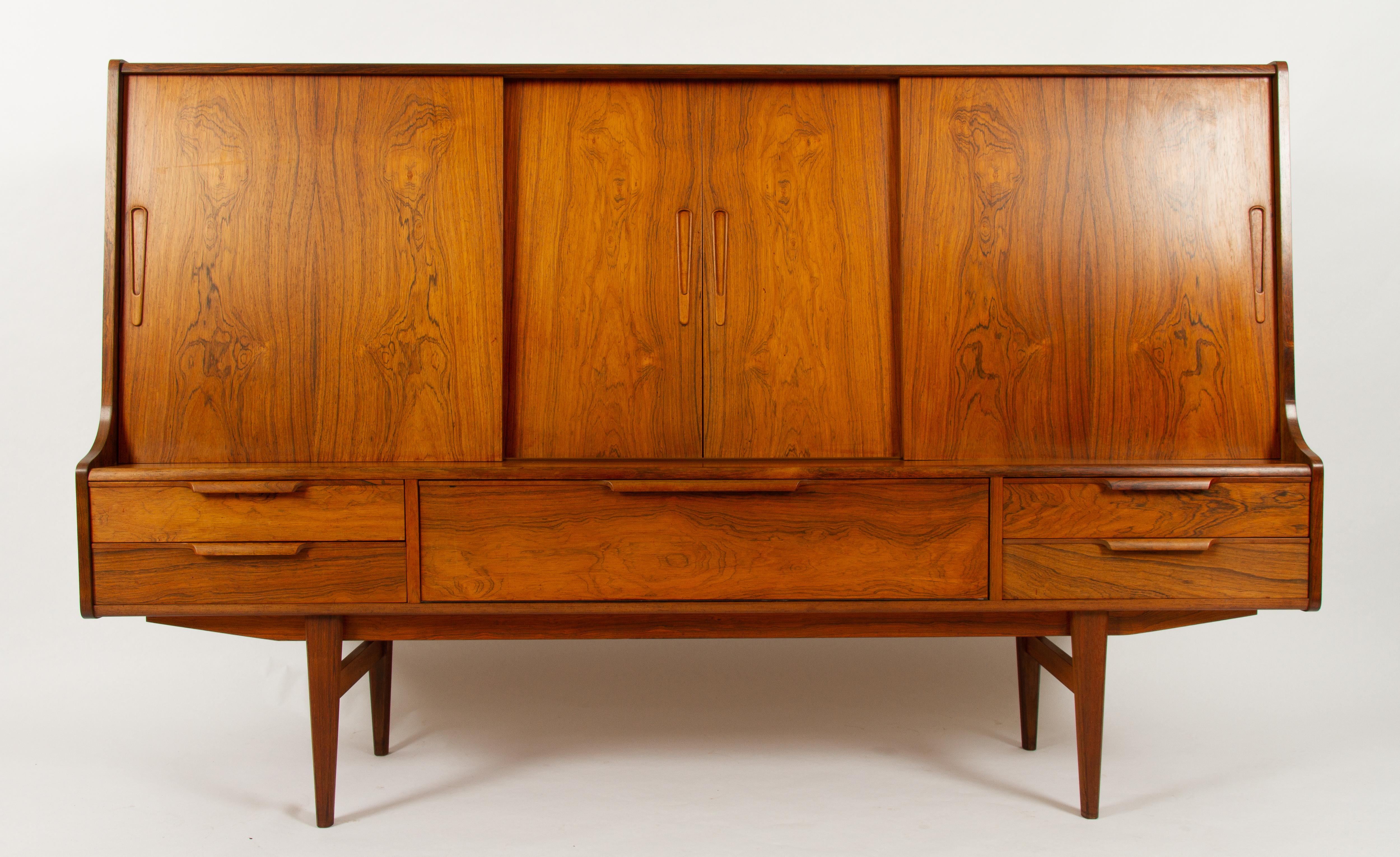 Vintage Danish rosewood sideboard, 1960s
Mid-Century Modern tall Rosewood credenza made in Denmark in the 1960s. Beautiful veneer with a golden hue and sculpted grips in solid rosewood. Mirrored bar unit with brass edged shelf and drawers with brass