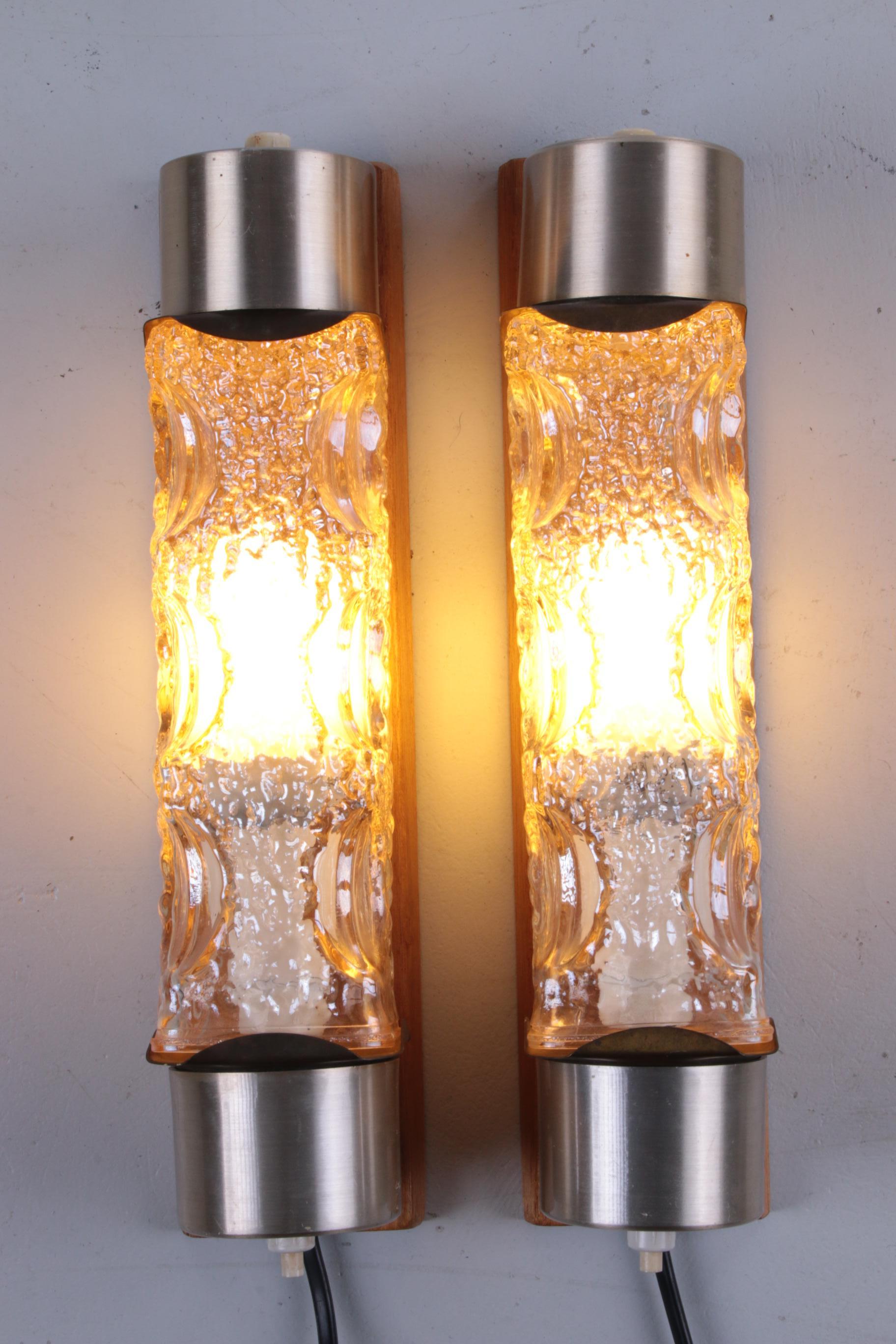 This is a beautiful and elegant set of vintage wall lamps. They are mounted on an oak shelf with two chrome covers and a thick glass shade in between that diffuses the light and gives of a wonderfull warm glow when the lamp is turned on.

The