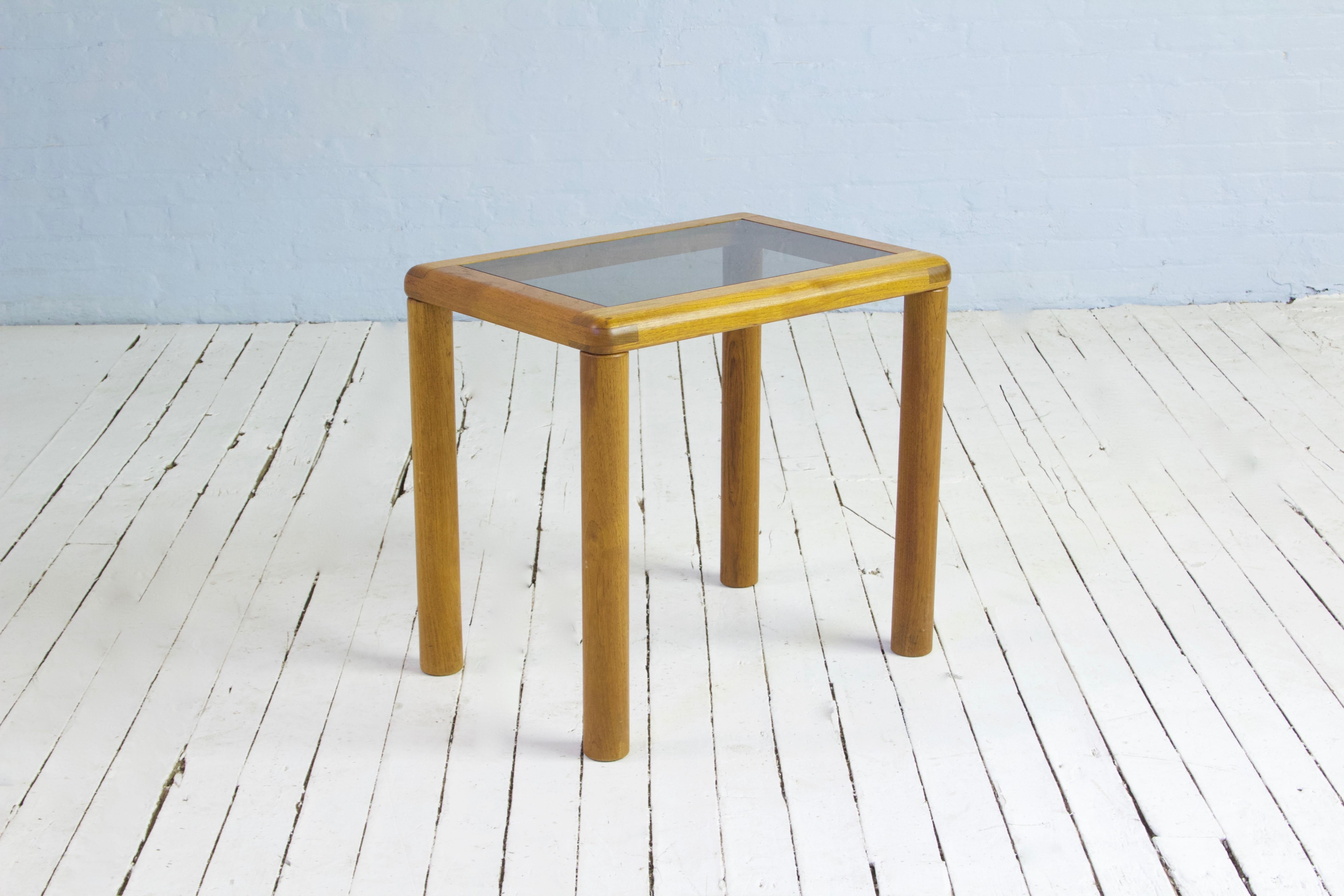 Vintage Danish side table in solid, patinated teak. Robust exposed joinery showcases the strength of this petite piece. Turned legs lend a playful appearance, while the tinted glass top and overall size make it the perfect table to accompany your