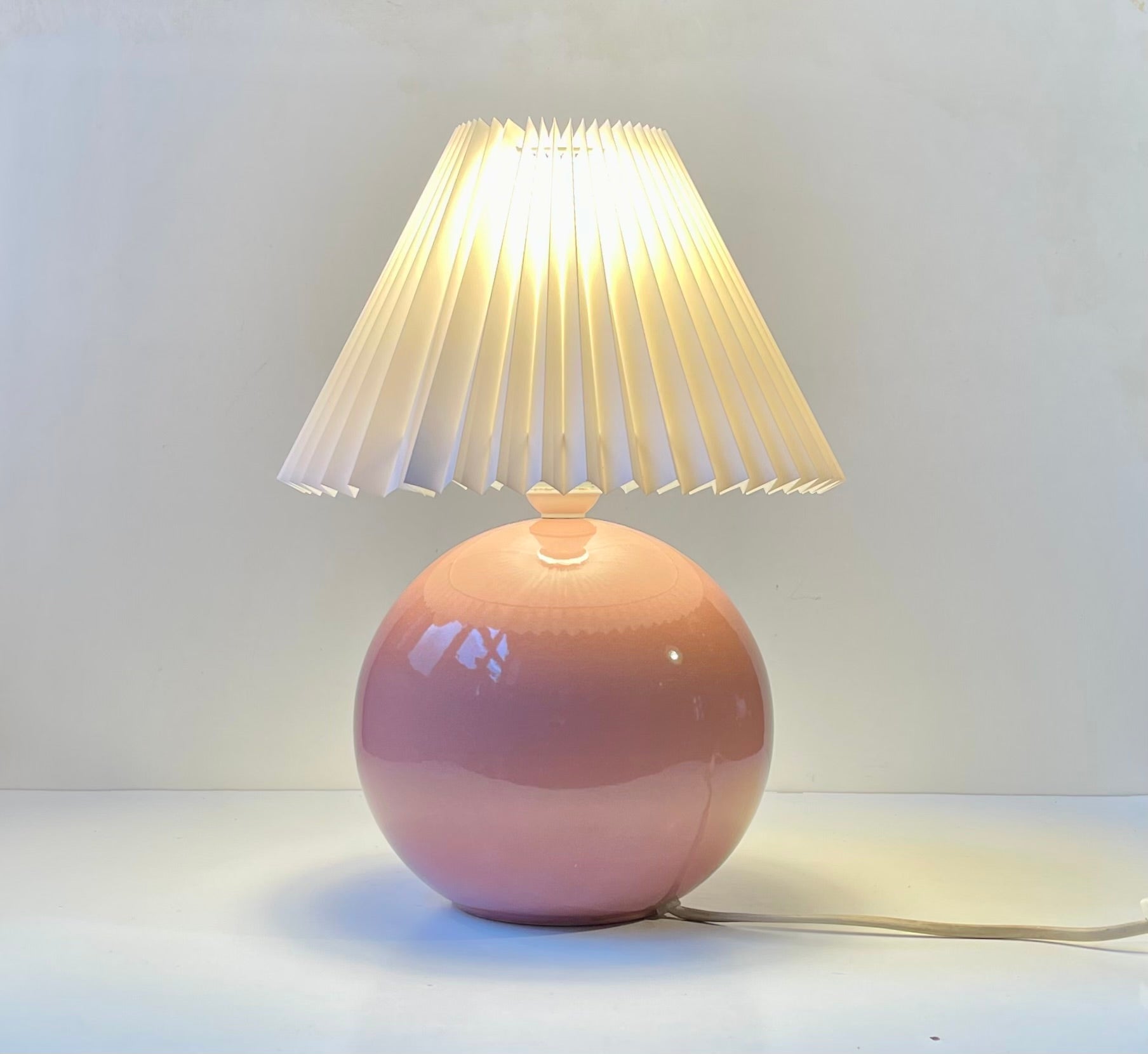 A 1980s Danish table light by Lamperiet Aarhus. The ceramic ball base features a monochrome pink glaze and the light comes installed with a fluted white shade. 

Measurements: H: 36 cm (with shade), Diameter: 26 cm (shade). 

Wellkept intact and