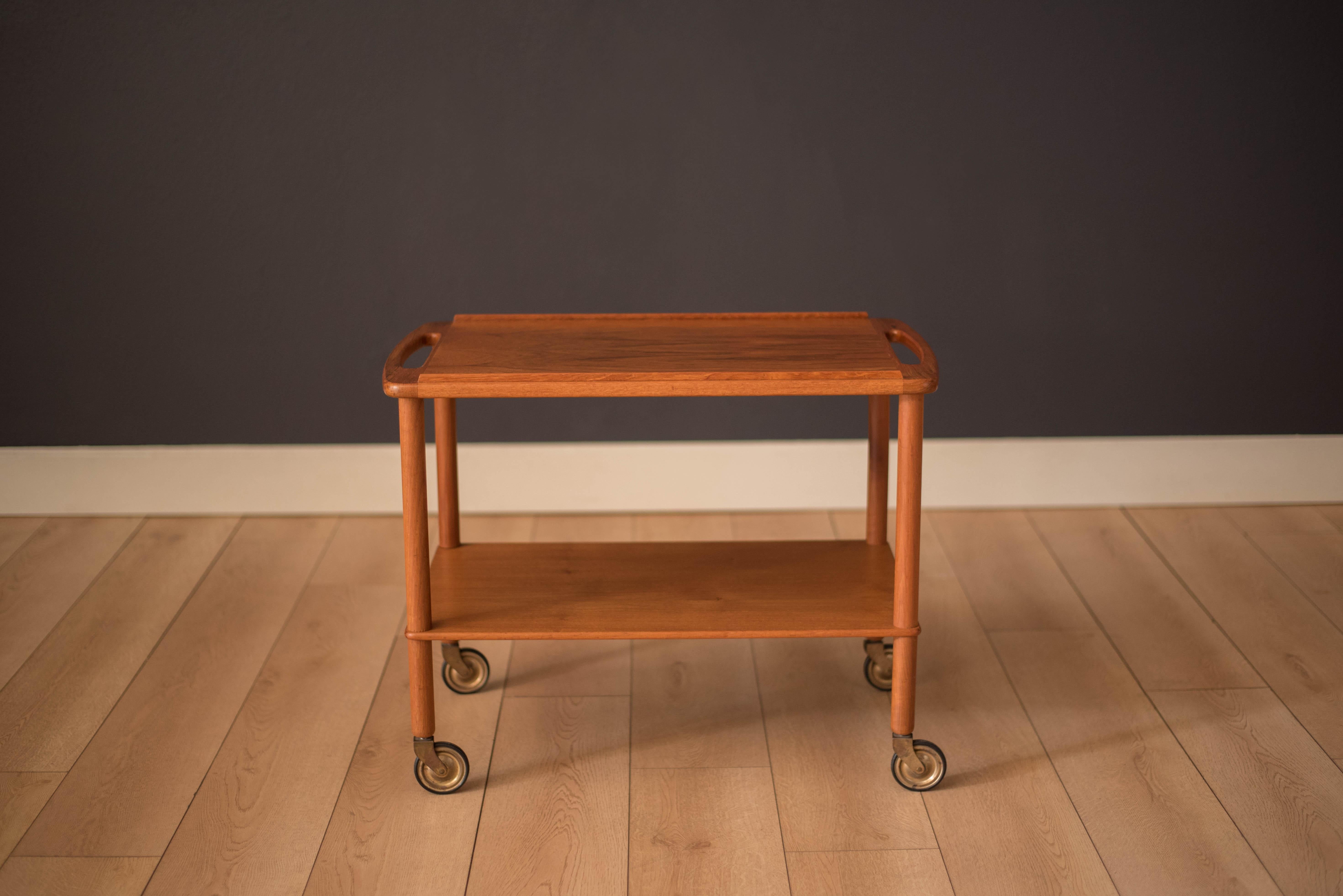Mid-Century Modern teak serving tea trolley or bar cart made by Bowa, Denmark, circa 1960s. This piece features two sculpted handles on each side and easy to roll original casters. Equipped with a lower tier shelf for extra display storage.