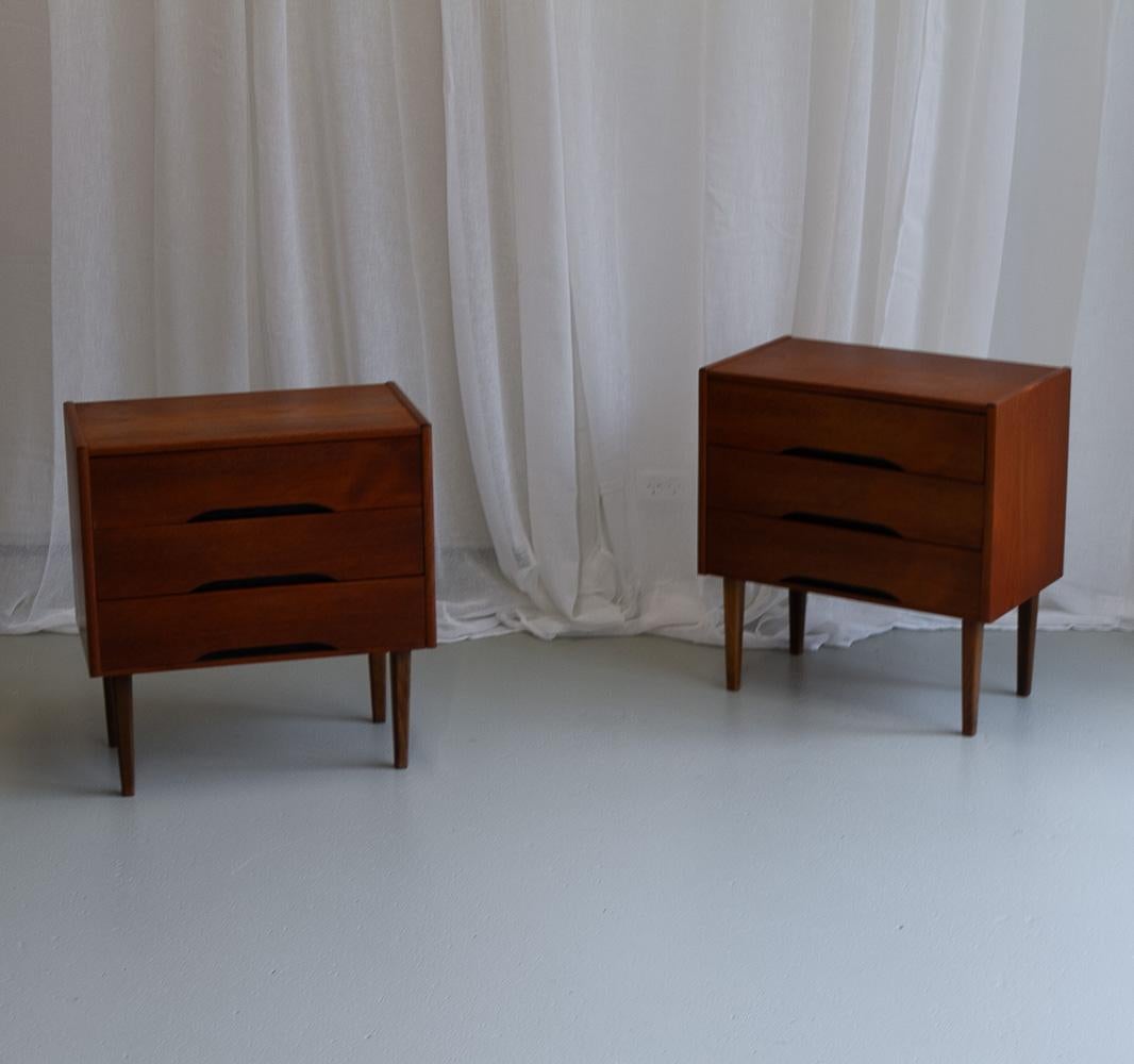 Vintage Danish Teak Bedside tables, 1960s. Set of 2.
Pair of nightstands in teak veneer with three drawers. Tapered legs in solid stained beech. Drawer fronts with black recessed pulls.

These small three drawer dressers are also suitable as side or