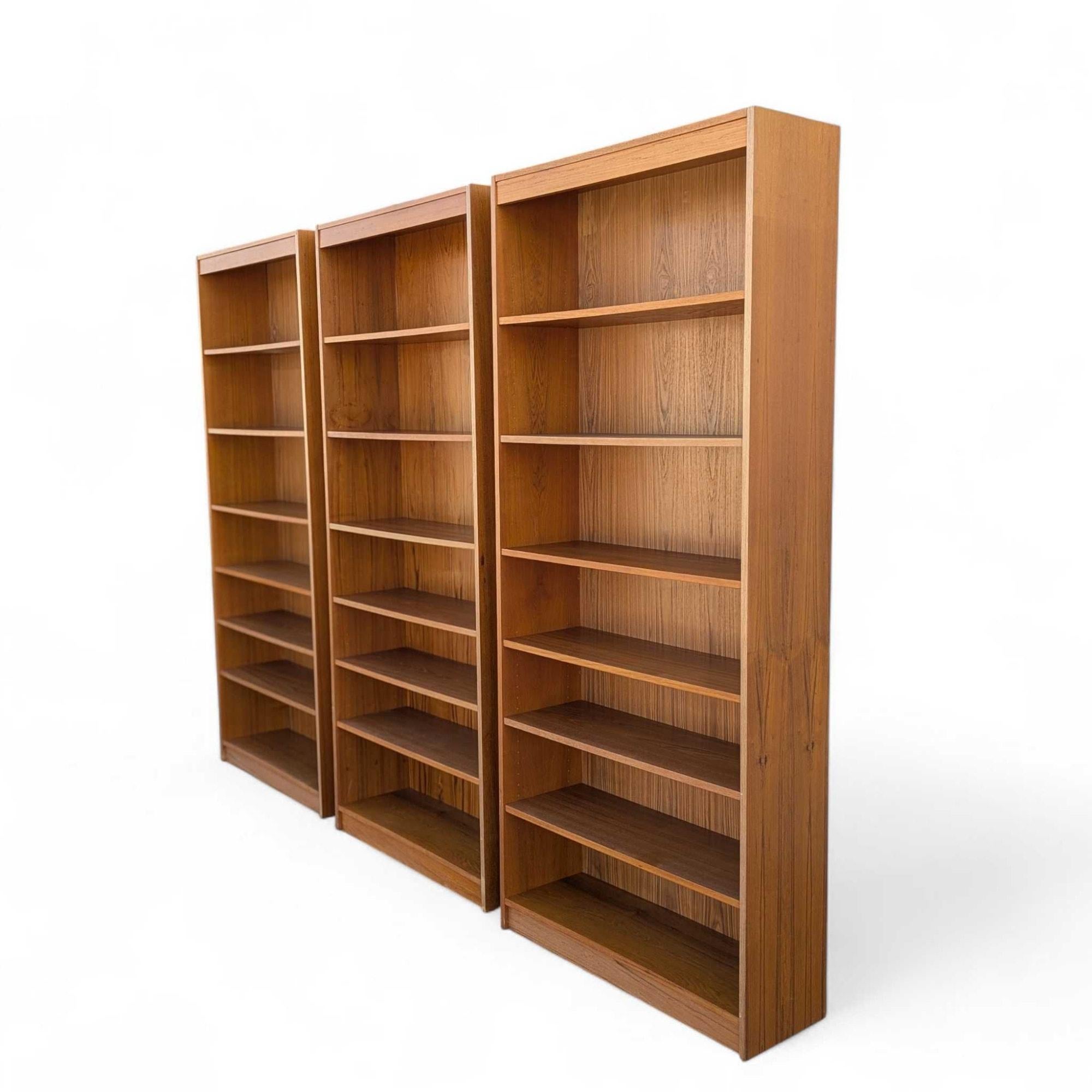 An elegant Set of Three Danish bookcases, crafted from teak veneer in a Mid-Century Modern style, featuring multiple shelves for ample storage and display.

Each bookcase is made from beautiful teak veneer, showcasing its characteristic grain. They
