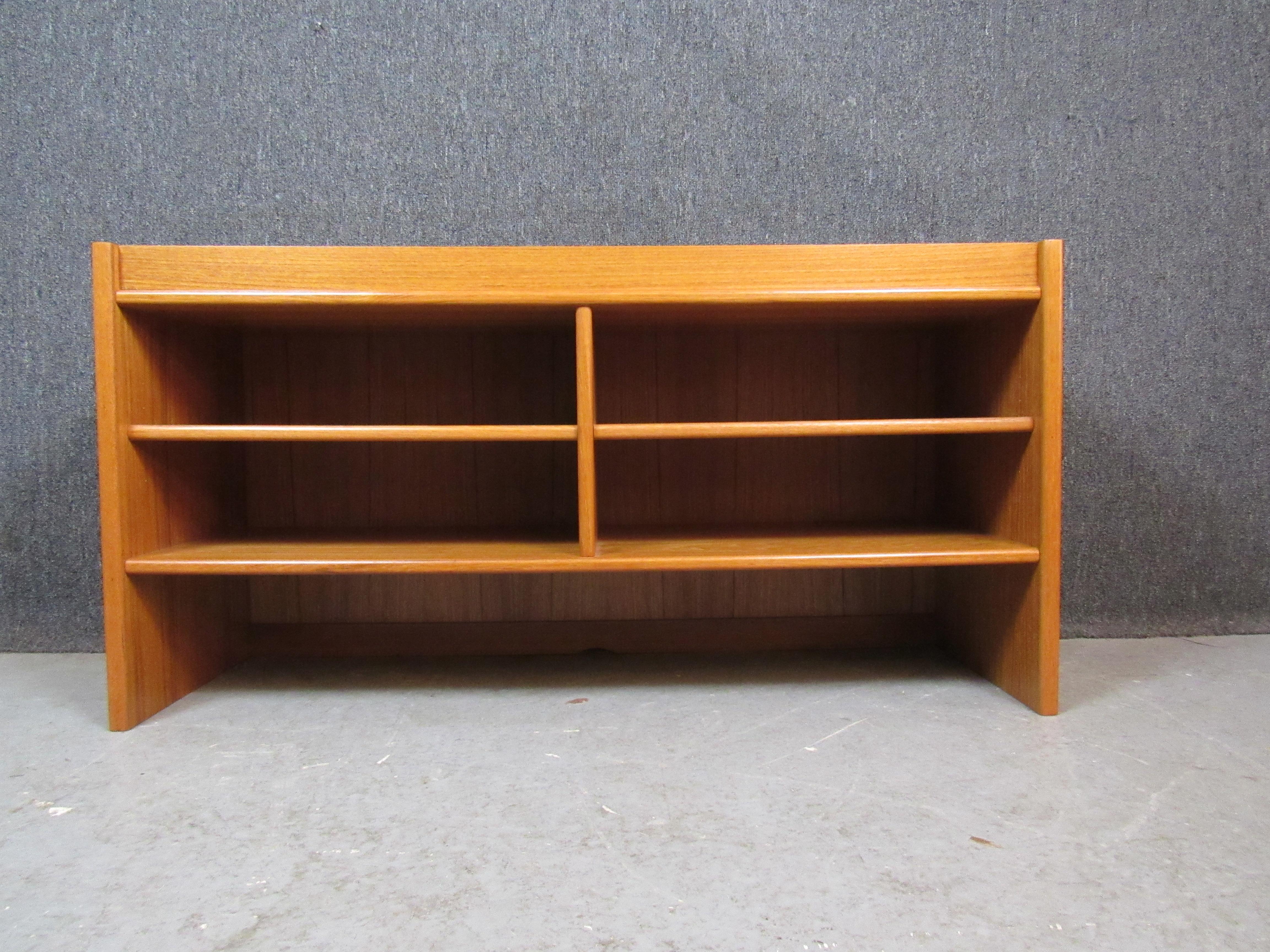 Give your space a dash of mid-century modern charm with this wonderful petite teak bookshelf. With minimalist lines, soft edges, and a vibrant swirling wood grain, this display case is sure to be an object of admiration in its own right. Four