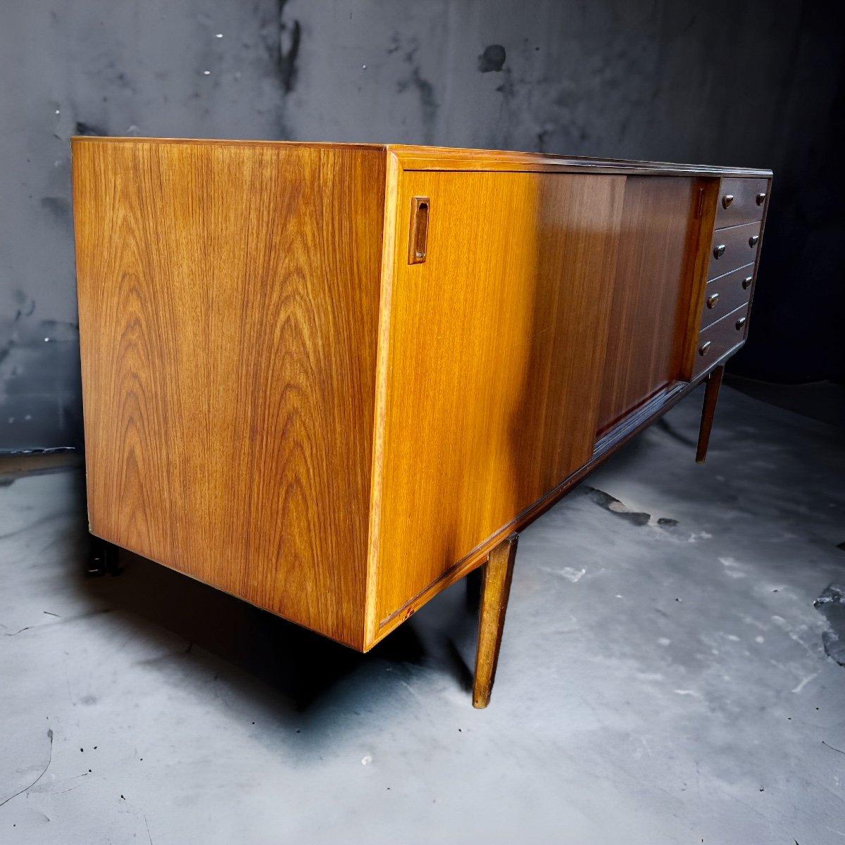 This very spacious and stylish vintage sideboard hailing from the 1960s boasts an authentic teak veneer finish in warm golden brown. It features two sliding doors that open to provide ample storage space despite its very light visual impression. On