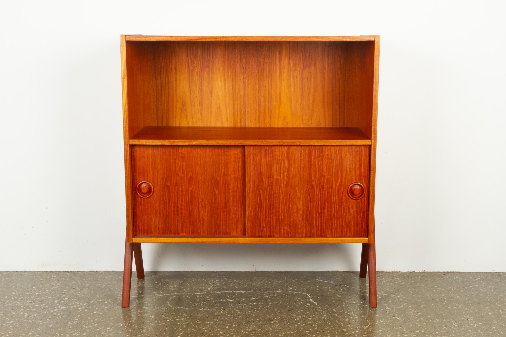 Vintage Danish teak cabinet, 1960s
Light and small elegant cabinet / bookcase in beautiful teak with a warm and golden hue. Top half with a wide open compartment, lower half with double sliding doors. Inside is a single shelf. Doors has round grips