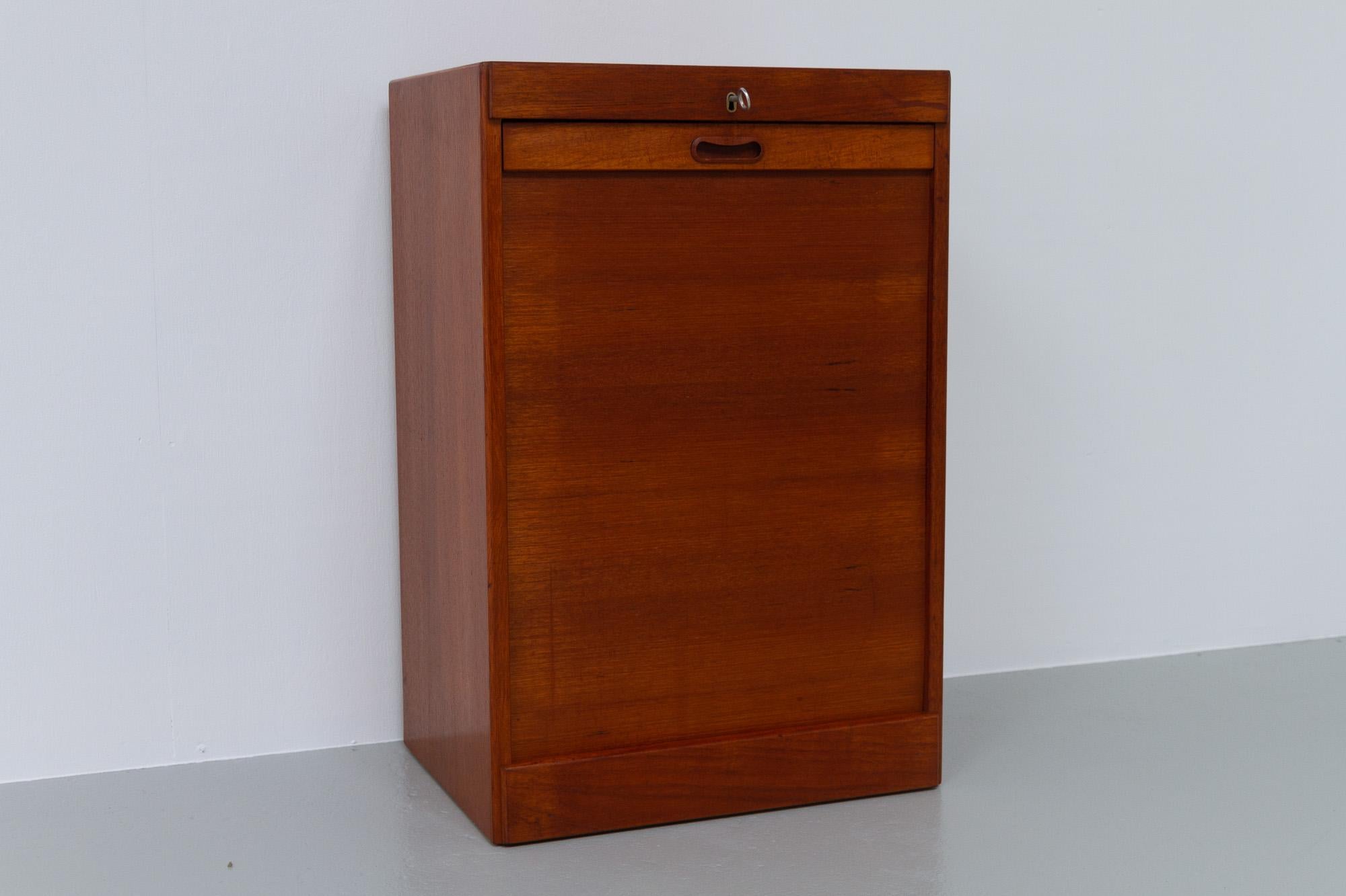 Vintage Danish teak cabinet with tambour door, 1960s.
Small Danish Mid-Century Modern filing cabinet in teak with vertical rolling tambour door. Three drawers in solid beech. Door is lockable, key is included. Sturdy construction.
Even though it