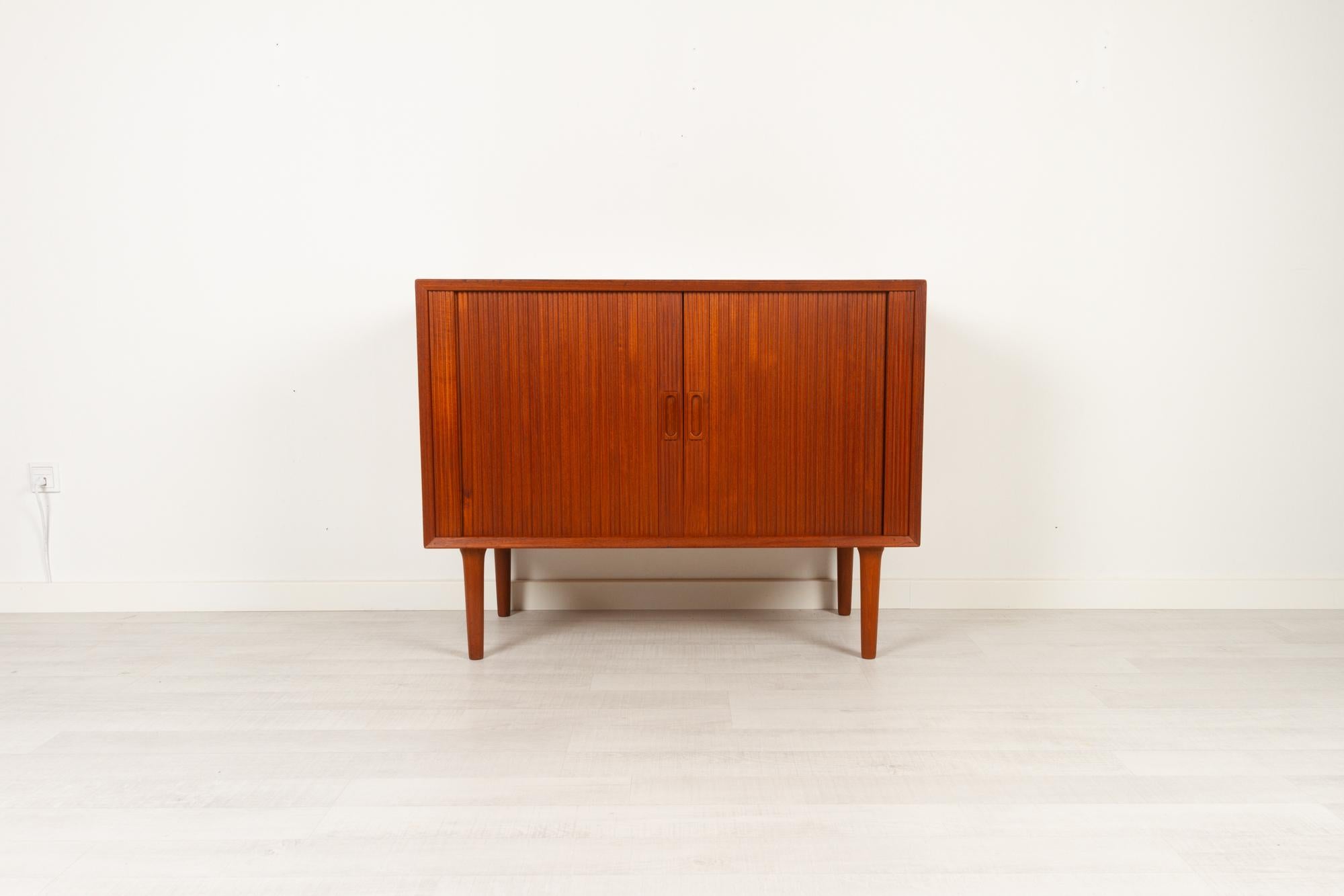 Vintage Danish teak cabinet with Tambour doors by Lyby Møbler, Denmark 1960s
Elegant and stylish Danish Mid-Century Modern cabinet with beautifully crafted tambour doors. Frame with bevelled edges and grips in solid teak. Round tapered legs with
