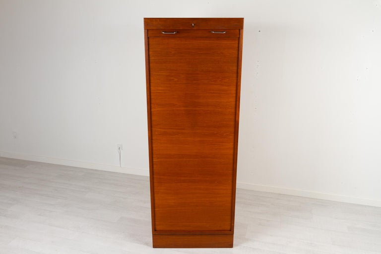 Vintage Danish teak cabinet with tambour front, 1960s
Tall Danish modern filing cabinet with vertical sliding tambour door in teak. 3 wide drawers and 2 shelves. Both shelves and drawers can be placed as desired. Rolling door opens with key. Key is
