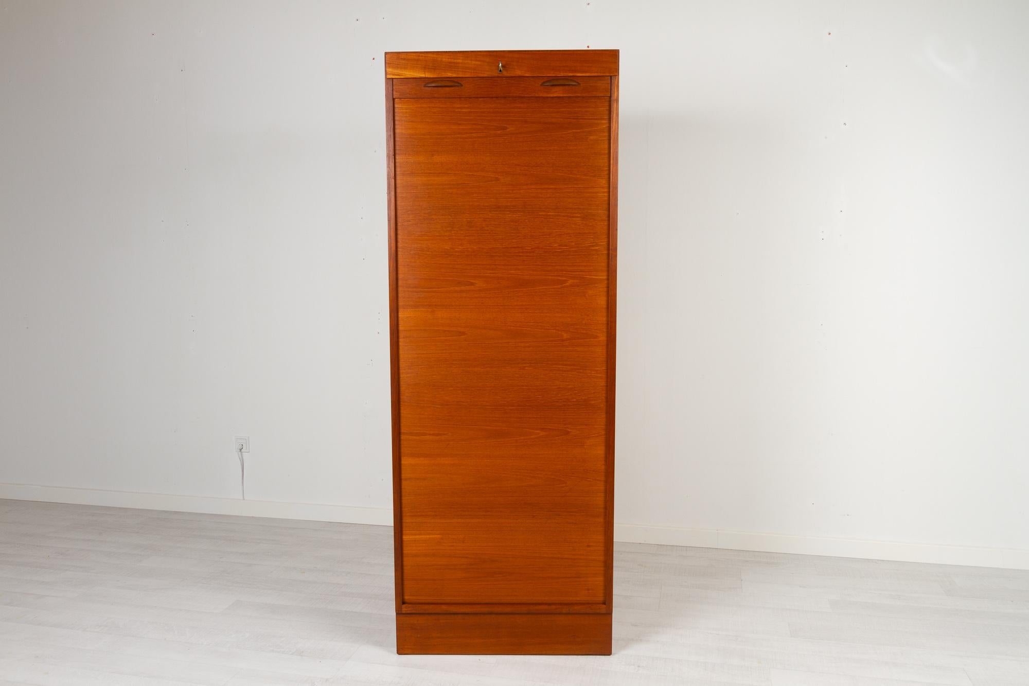Vintage Danish teak cabinet with tambour front, 1960s
Tall Danish modern filing cabinet with vertical sliding tambour door in teak. 4 wide drawers and 1 shelf. Both shelf and drawers can be placed as desired. Rolling door opens with key. Key is