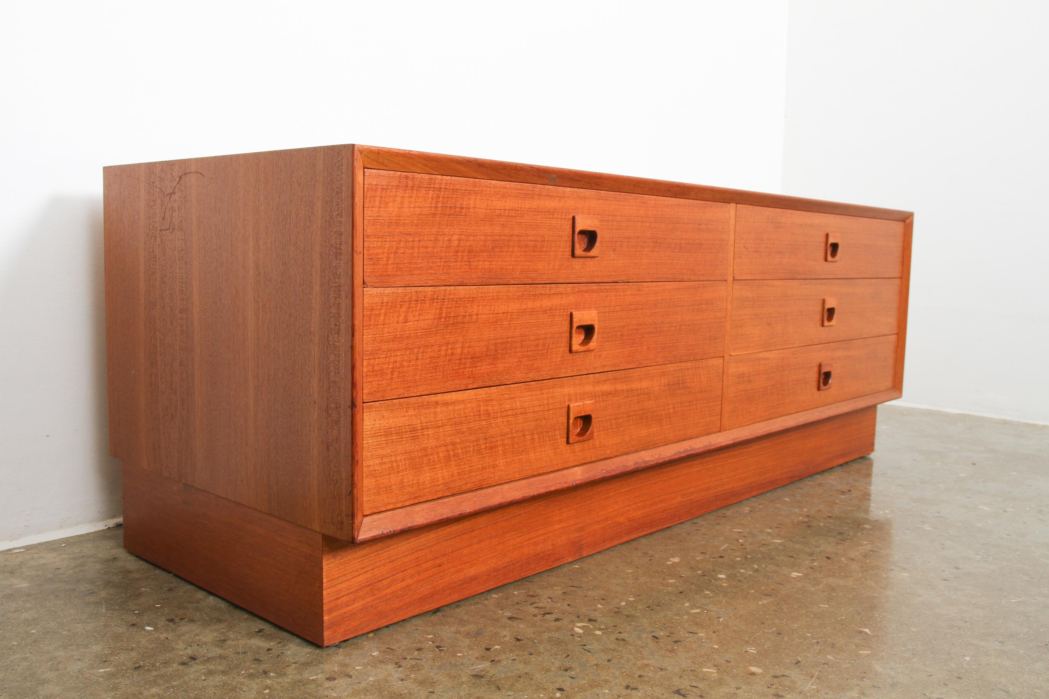 This low and wide Danish midcentury chest of drawers features six large drawers and sits on a frame. It can support a heavy TV, in the hallway as a bench or as a sideboard. Loads of storage space. Beautiful teak veneer and elegant grips in solid