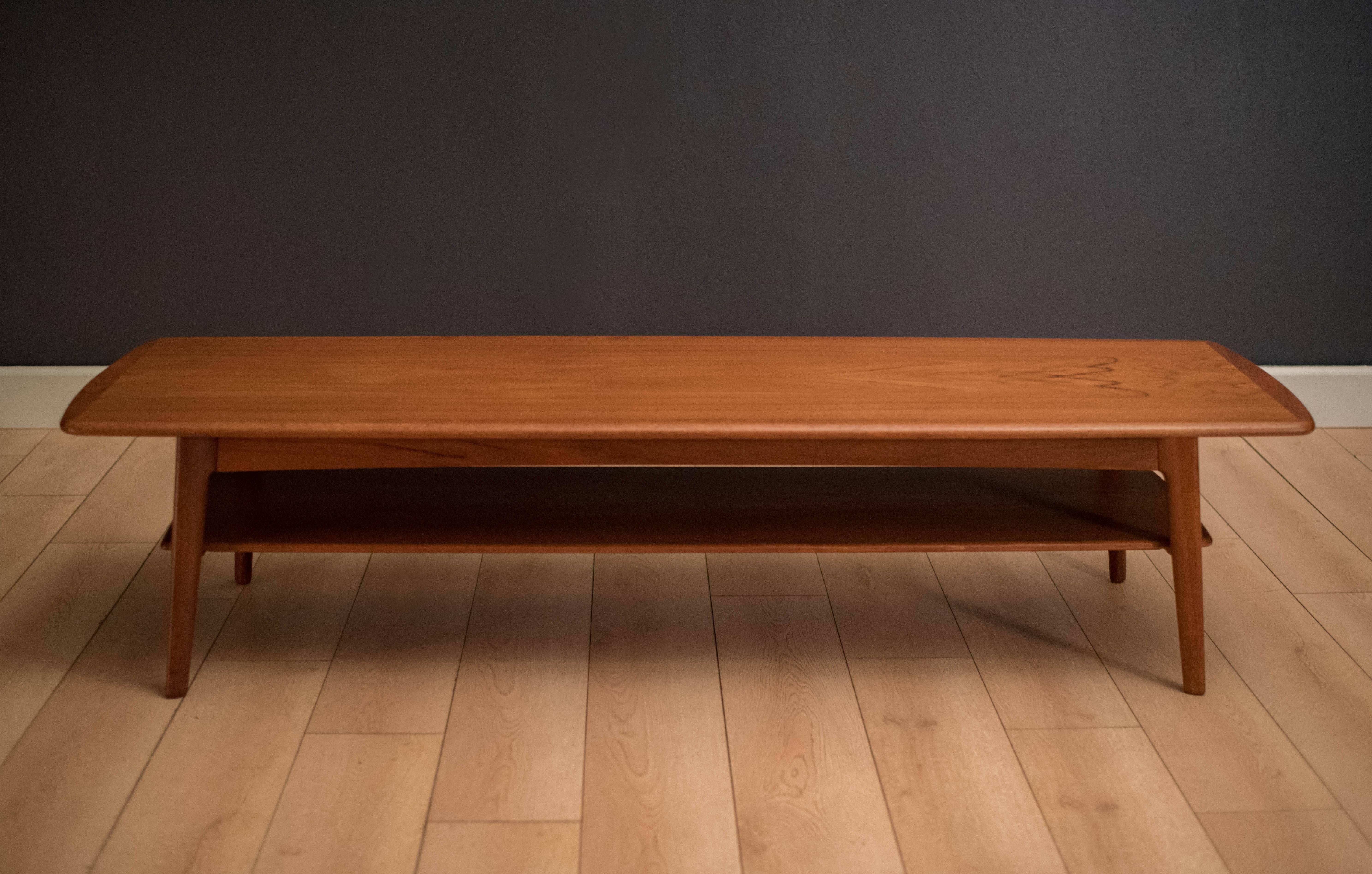 Mid-Century Modern long coffee table designed by Svend Aage Madsen for Karl Lindegaard Møbelfabrik in teak. This piece features solid sculpted edges and splayed tapered legs. Includes a lower tier display shelf.