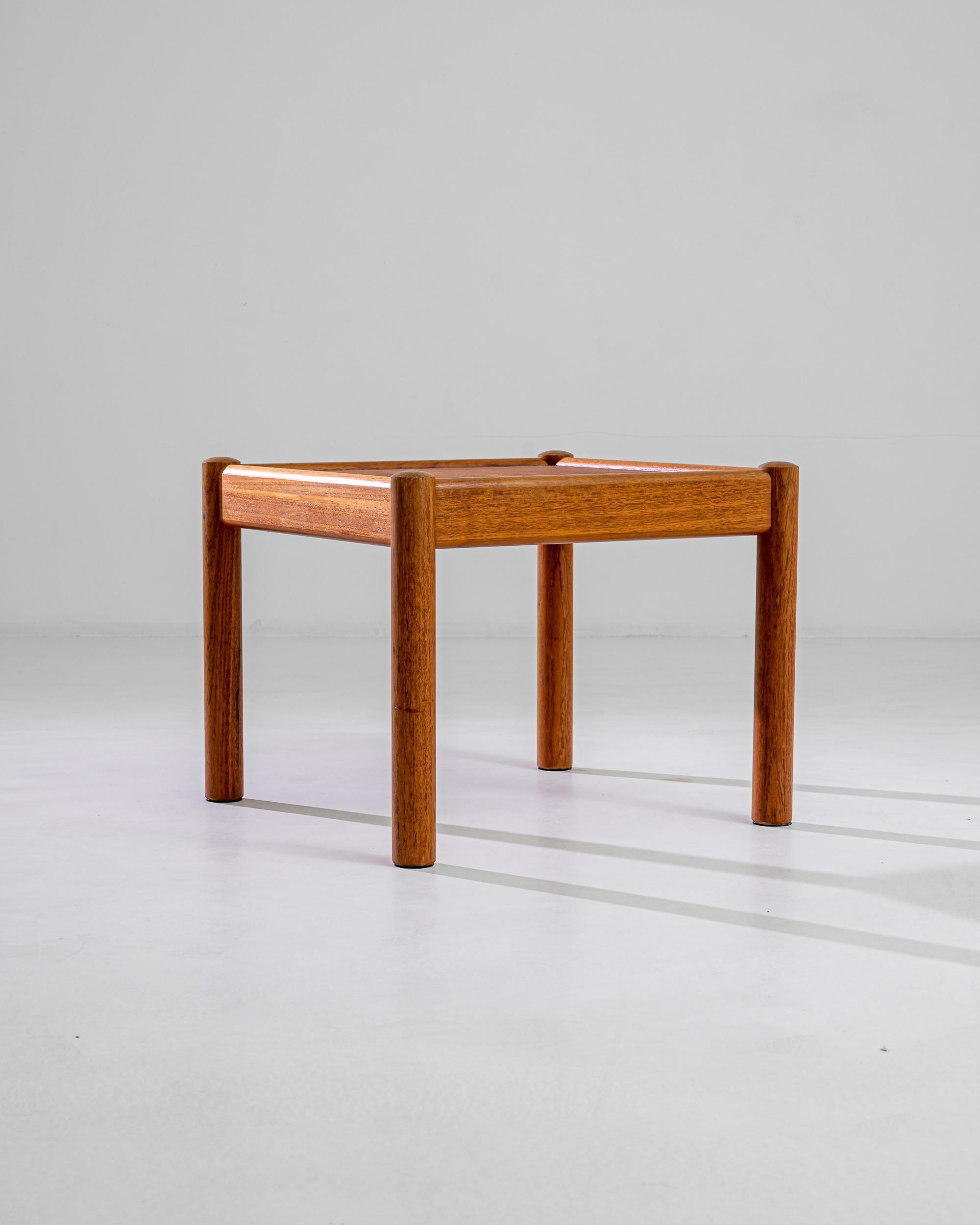 This minimalist Danish coffee table charms with the simple elegance of its outlines: sturdy round feet are attached to a sleek apron that frames the perfectly square table top in a natural way. The tawny hue of the teak endows this 20th century