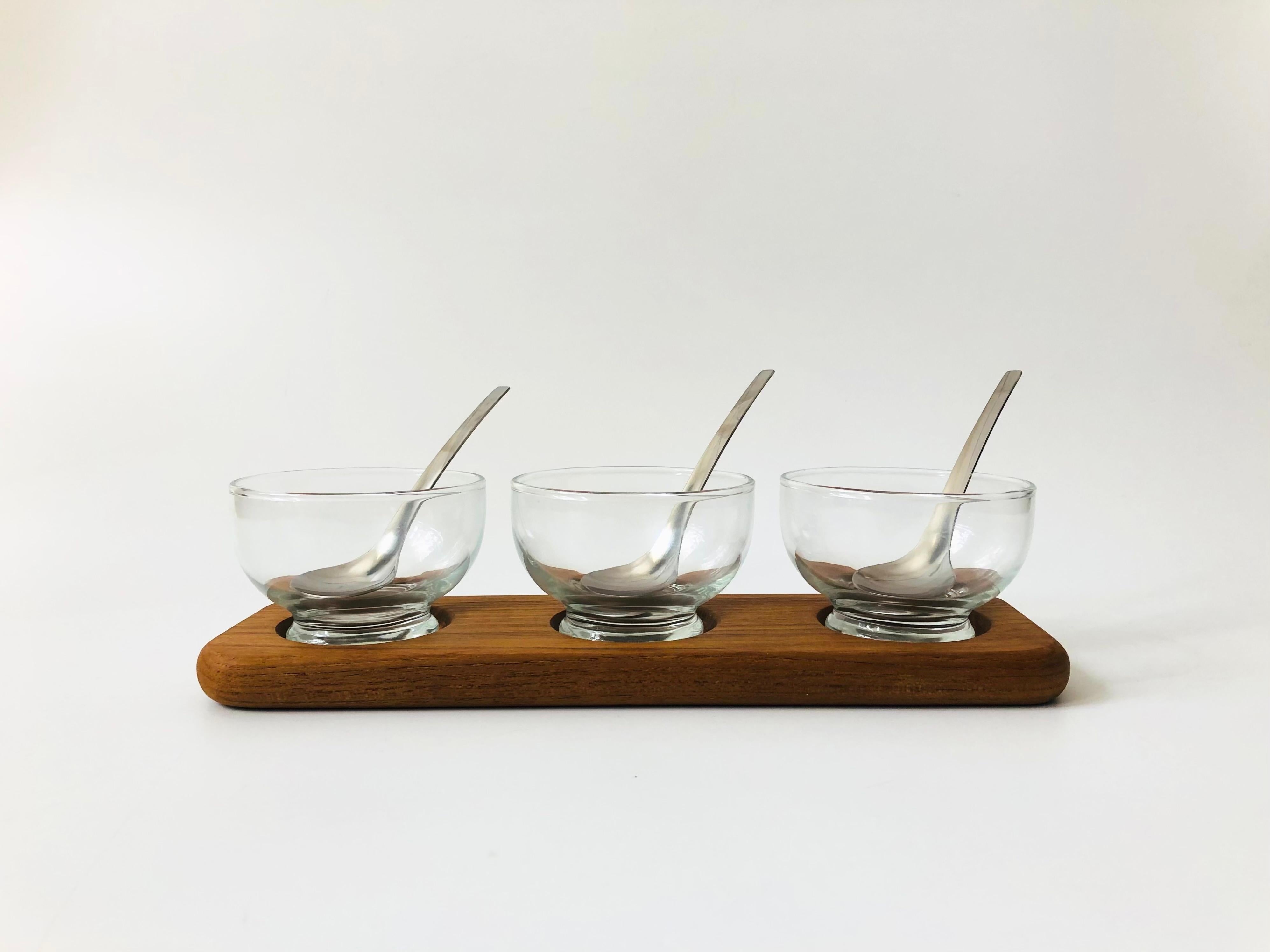 A vintage Danish condiment set by Selandia designs. Includes 3 glass bowls and 3 stainless steel spoons that fit neatly on a teak tray with recessed areas for holding the bowls. Perfect for serving sauces, condiments, or snacks.