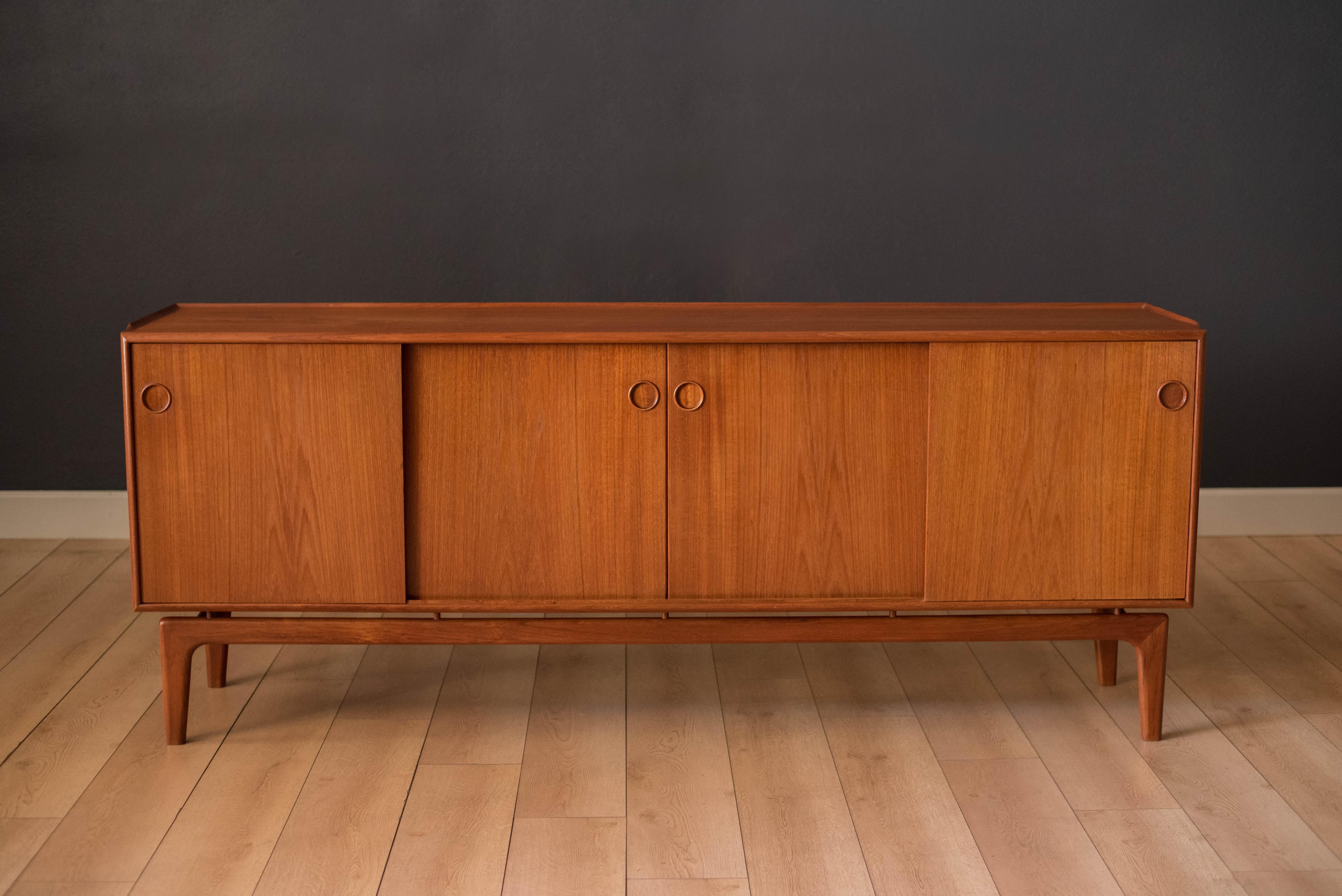 Mid-Century Modern sideboard credenza in teak designed by Arne Hovmand-Olsen for Mogens Kold. This piece features a unique floating base with sculpted details. Includes five dovetailed drawers and three fixed shelves enclosed with sliding doors that