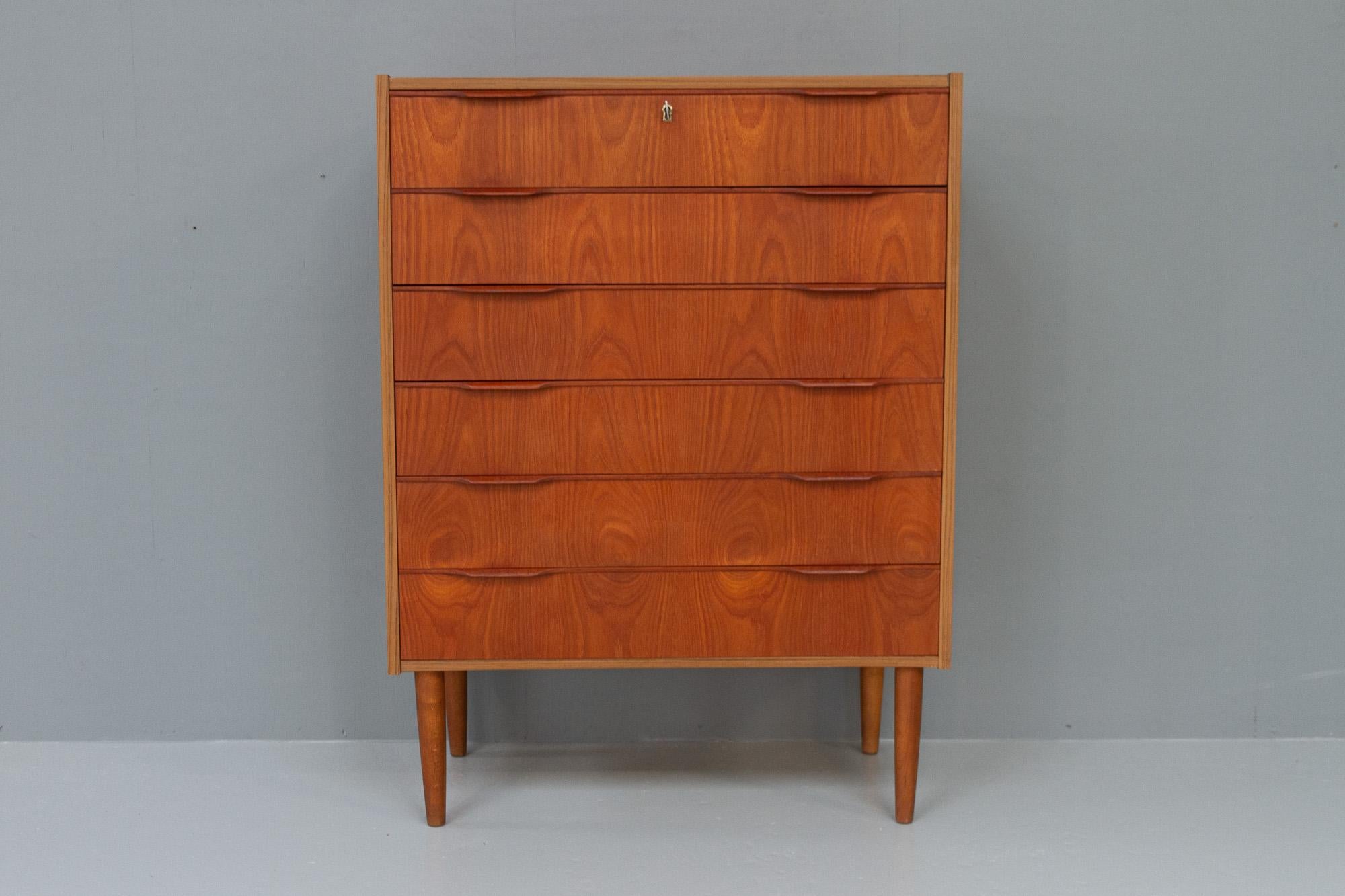Vintage Danish Teak dresser, 1960s.
Danish Modern chest of drawers in veneered teak. Round tapered legs in stained solid beech. Six drawers with sculpted pulls in solid teak. Top drawer with a lock, key is included.
Made in Denmark in the