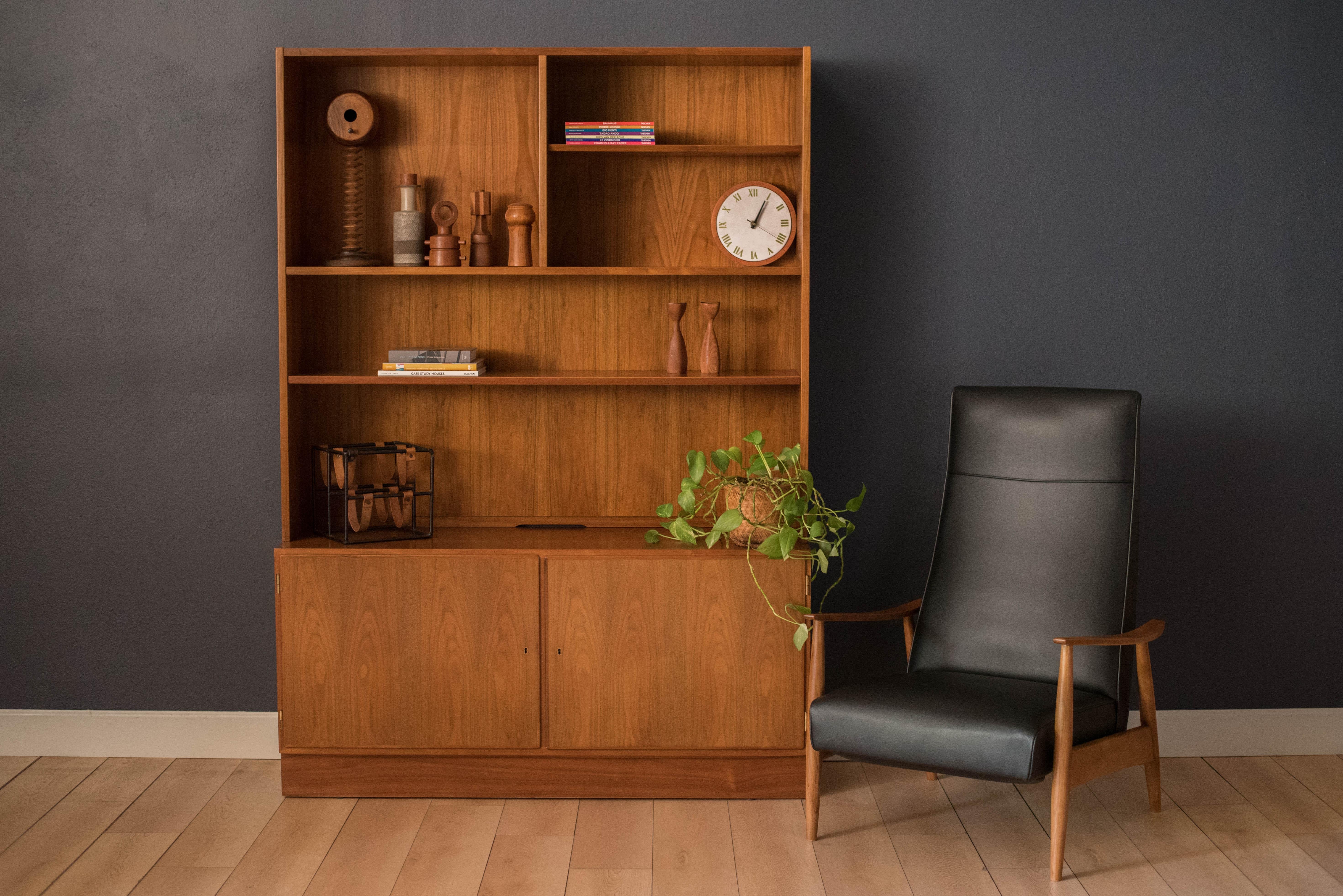 Mid-Century Modern bookcase and cabinet designed by Carlo Jensen for Hundevad & Co. in teak. This cabinet features double locking doors that reveal three drawers and open storage space with adjustable shelving. Bookshelf display easily detaches from