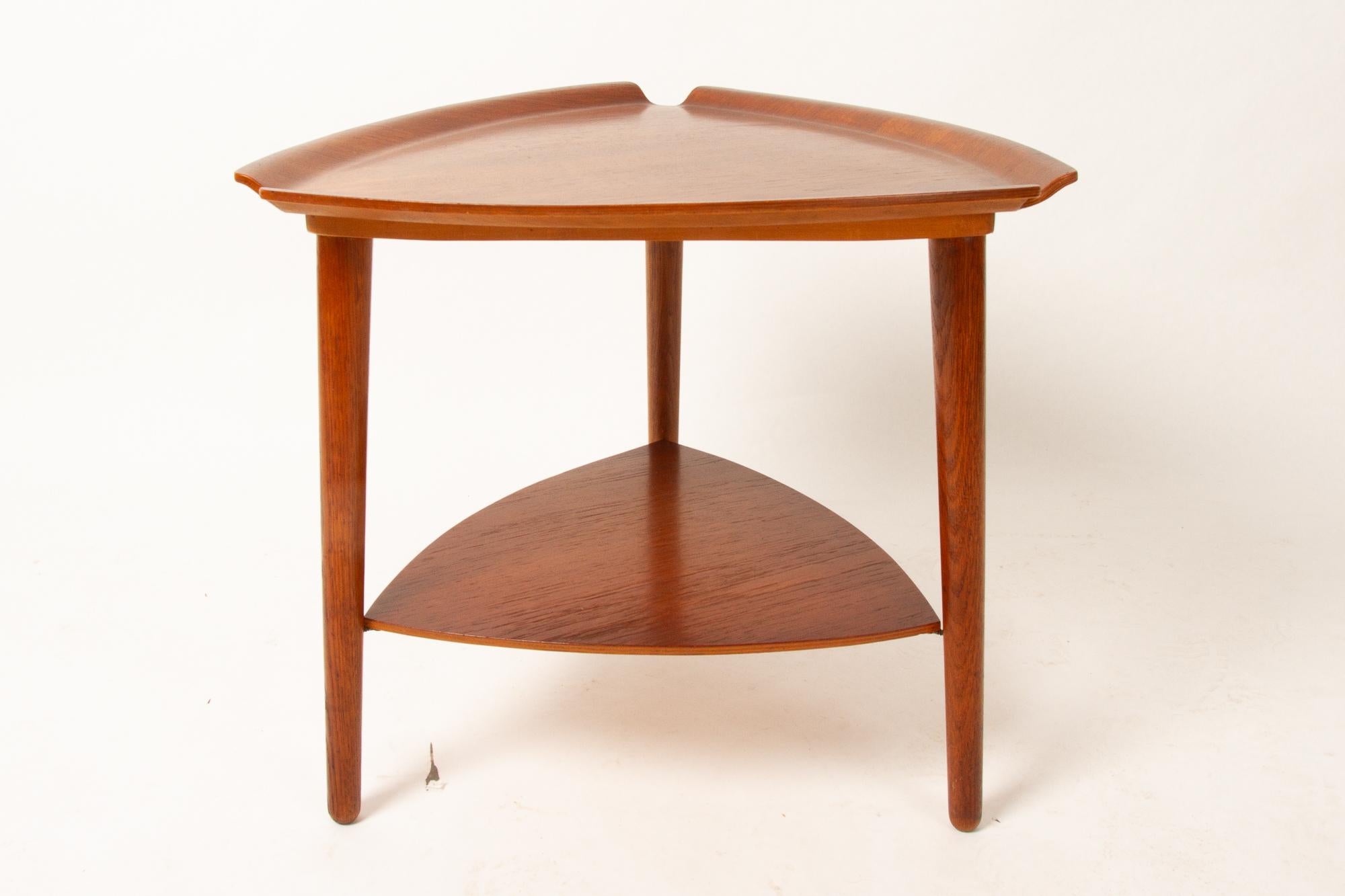 Vintage Danish teak side table 1960s.
Triangular side table with shelf. Table top teak veneered plywood with curved and flared edges, round cut-outs in each corner. Legs in solid oak.
Very good vintage condition. Cleaned, oiled and varnished.