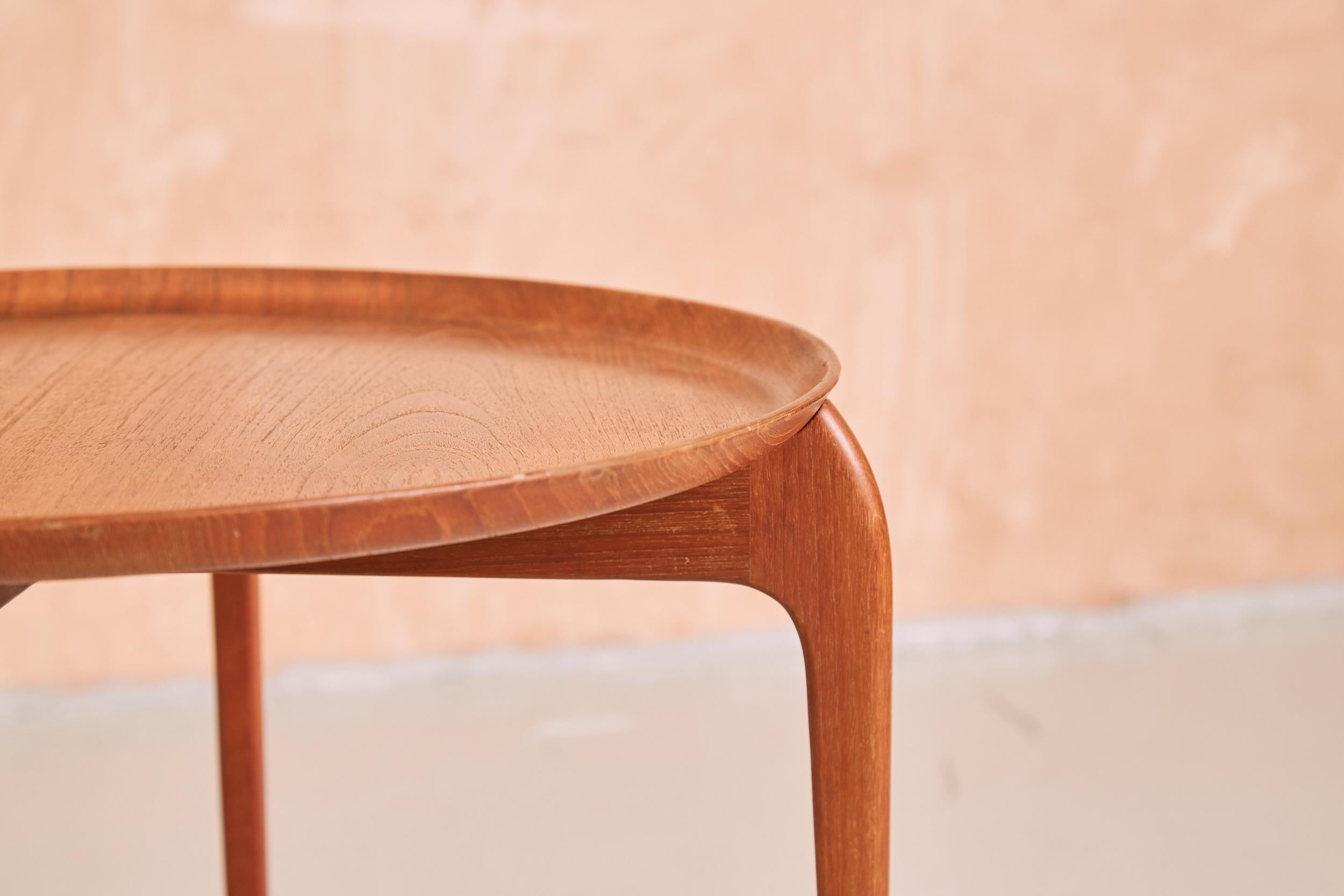 An elegant Danish mid century side table which doubles as a serving tray. The circular teak tray curves up at the edges for practicality but retains a delicate refined design, sitting on the haunches of the base, forming the top of four tapered