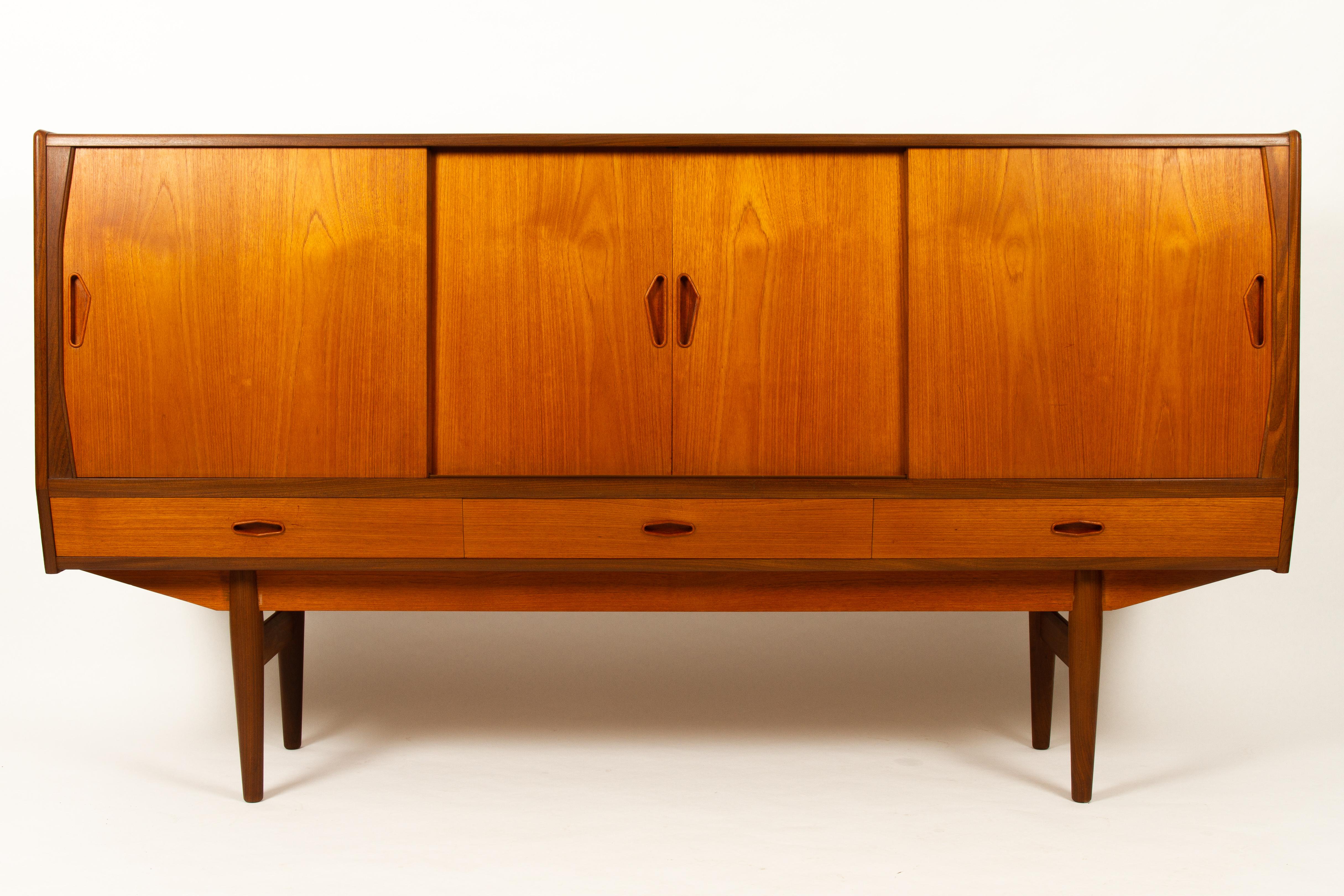 Vintage Danish teak sideboard, 1960s
Mid-Century Modern tall teak credenza made in Denmark in the 1960s. Beautiful veneer with a golden hue and sculpted grips in solid teak. Mirrored bar unit with curved shelf and drawers with brass handles. Two