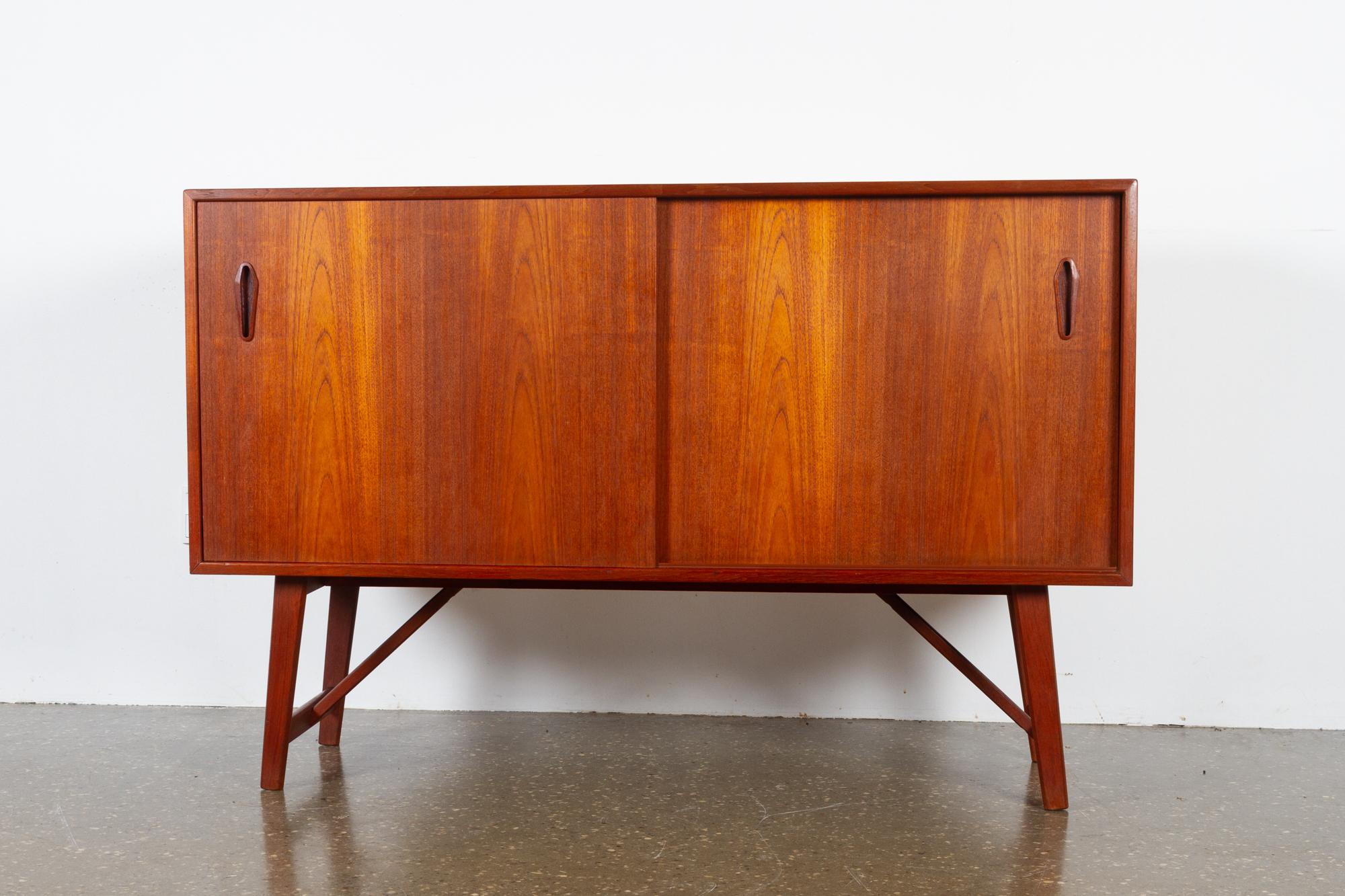 Vintage Danish teak sideboard, 1960s
Small and elegant Mid-Century Modern lowboard with double sliding doors and shelves.
Very nice warm and golden veneer color. Sculpted grips in solid teak. Slightly slanted legs. Frame and legs in solid teak. A