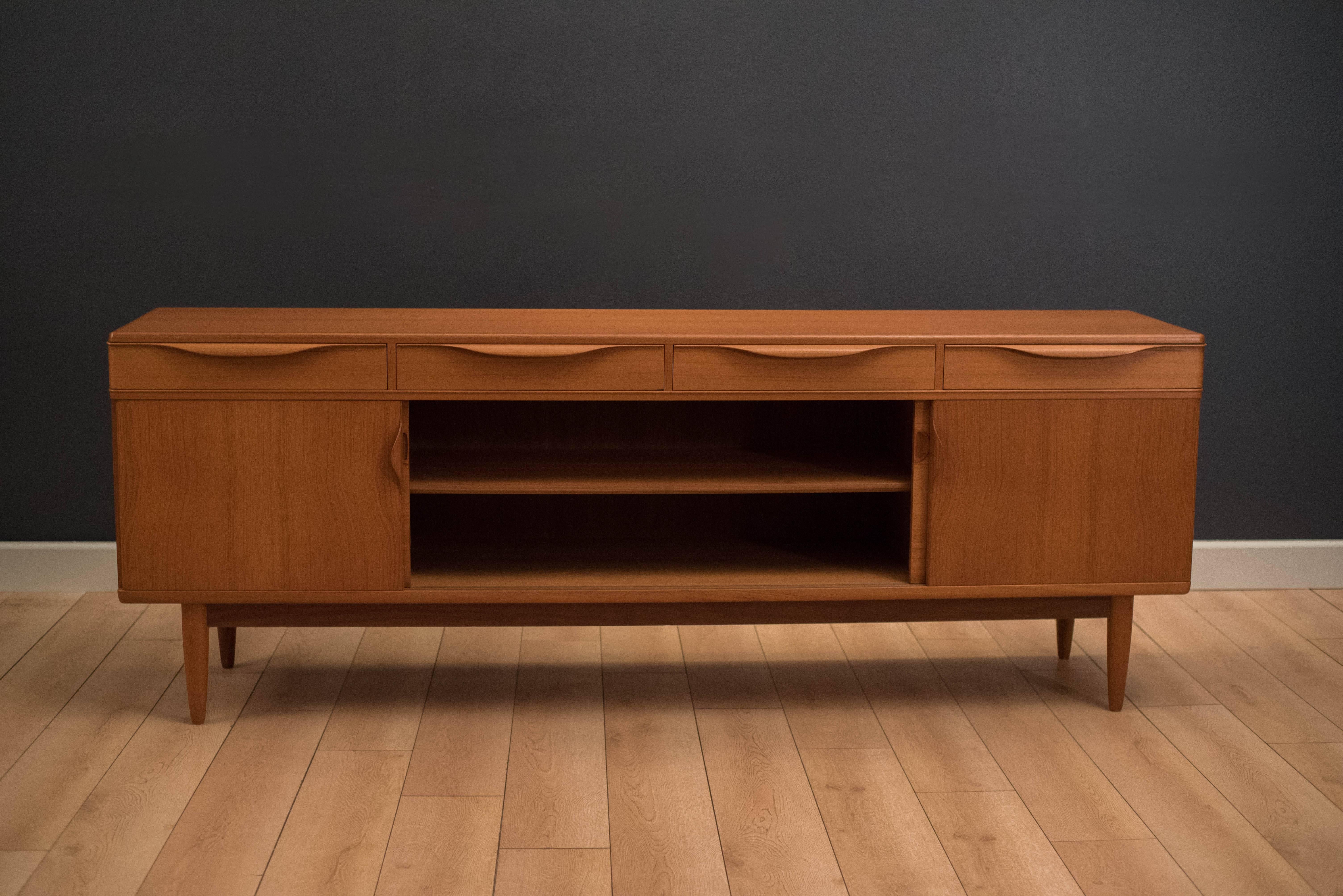 Mid-Century Modern credenza in teak manufactured by Bramin. This statement piece features unique curved corner edging and four dovetailed drawers with sculpted wood handles. Equipped with sliding doors that contain open storage space with adjustable