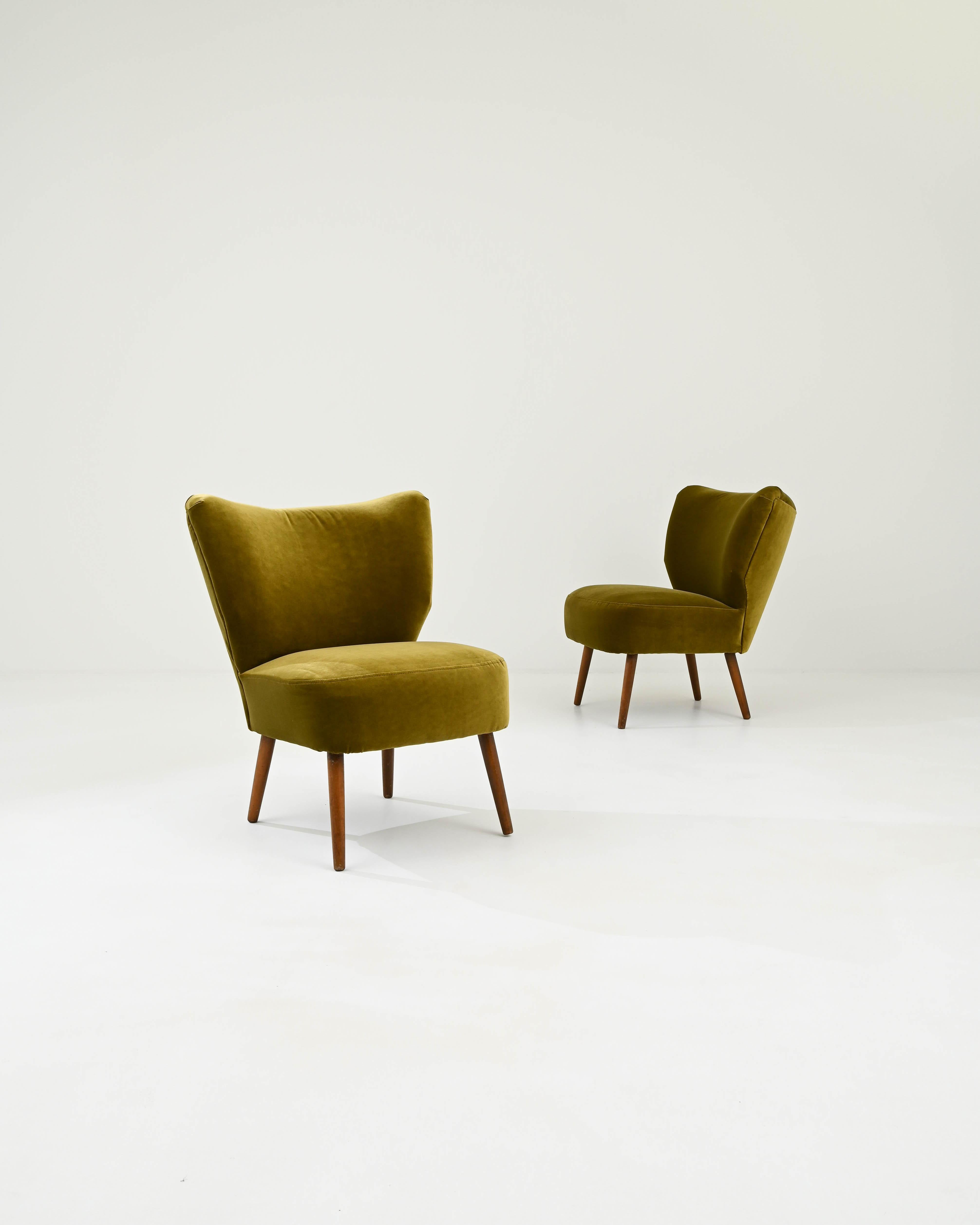 A pair of velvet upholstered lounge chairs made in 1950s Denmark. Characteristic of mid-20th century Danish design, this pair of ornate armchairs impart a sense of chic poise as well as inviting comfort. The hardwood legs have a lovely vintage