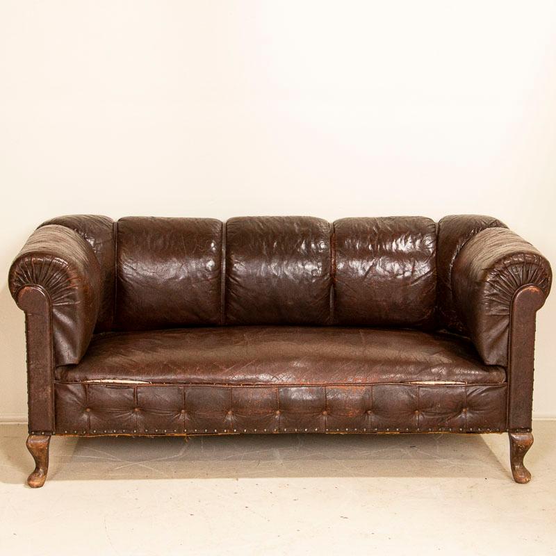 Vintage leather has an appeal all its own, even when worn and weathered as much as this old sofa. The heavily rolled arms and back are accented by straps of leather, several of which are loose and need to be tacked/sewn back down. The aged patina of