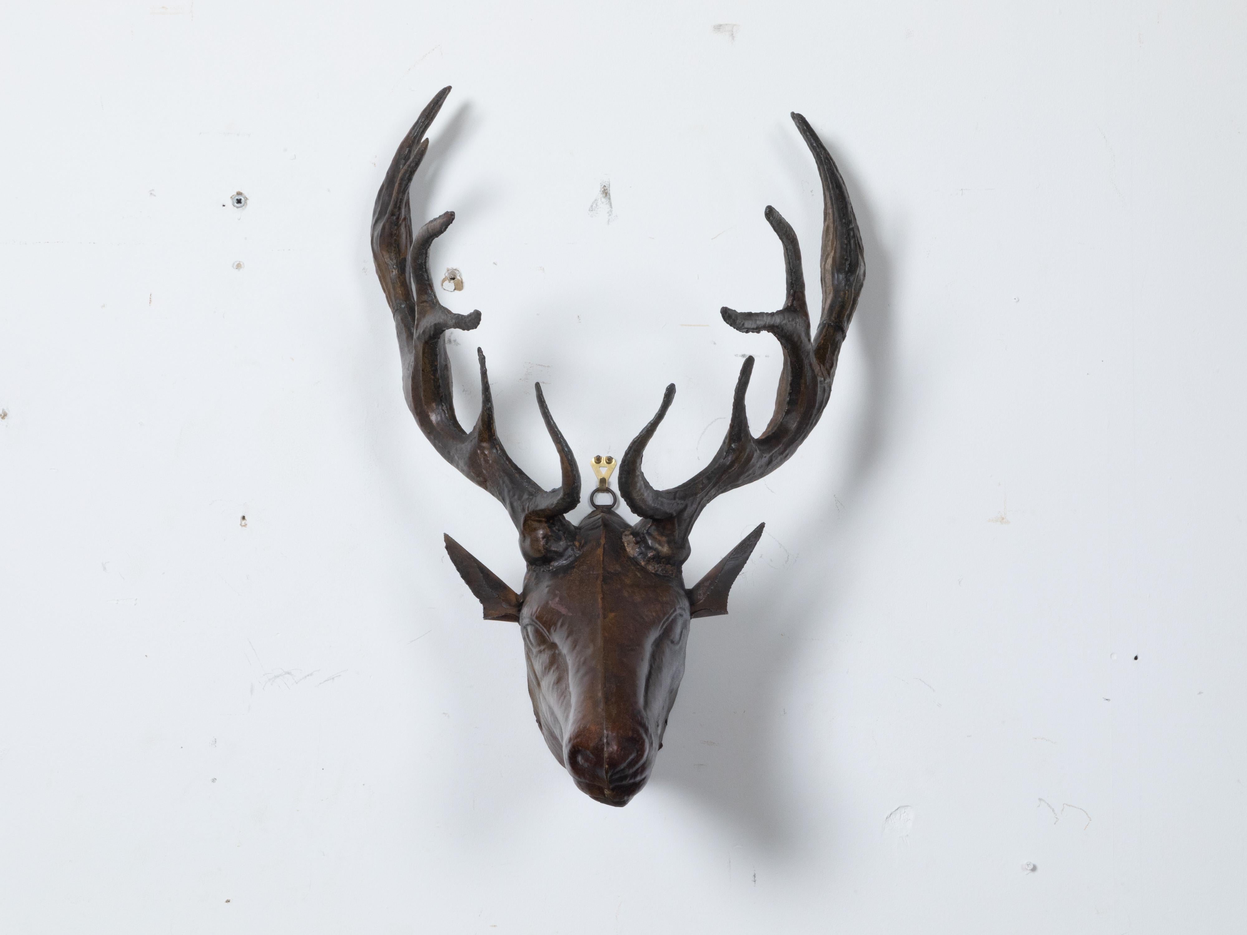 A vintage painted tôle stag head wall mounted sculpture with large antlers, brown patina and wooden board. Captivate your space with this vintage painted tôle stag head wall sculpture, a striking piece that harmoniously blends art and nature.