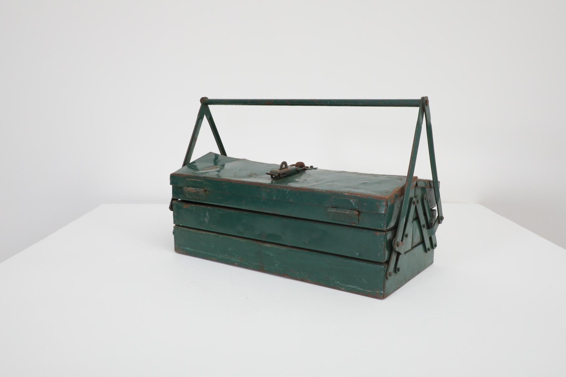 Vintage green metal tool box with handle and stacking trays. In original condition with visible wear, including enameled loss, discoloration and scratches. Wear is consistent with its age and use.
