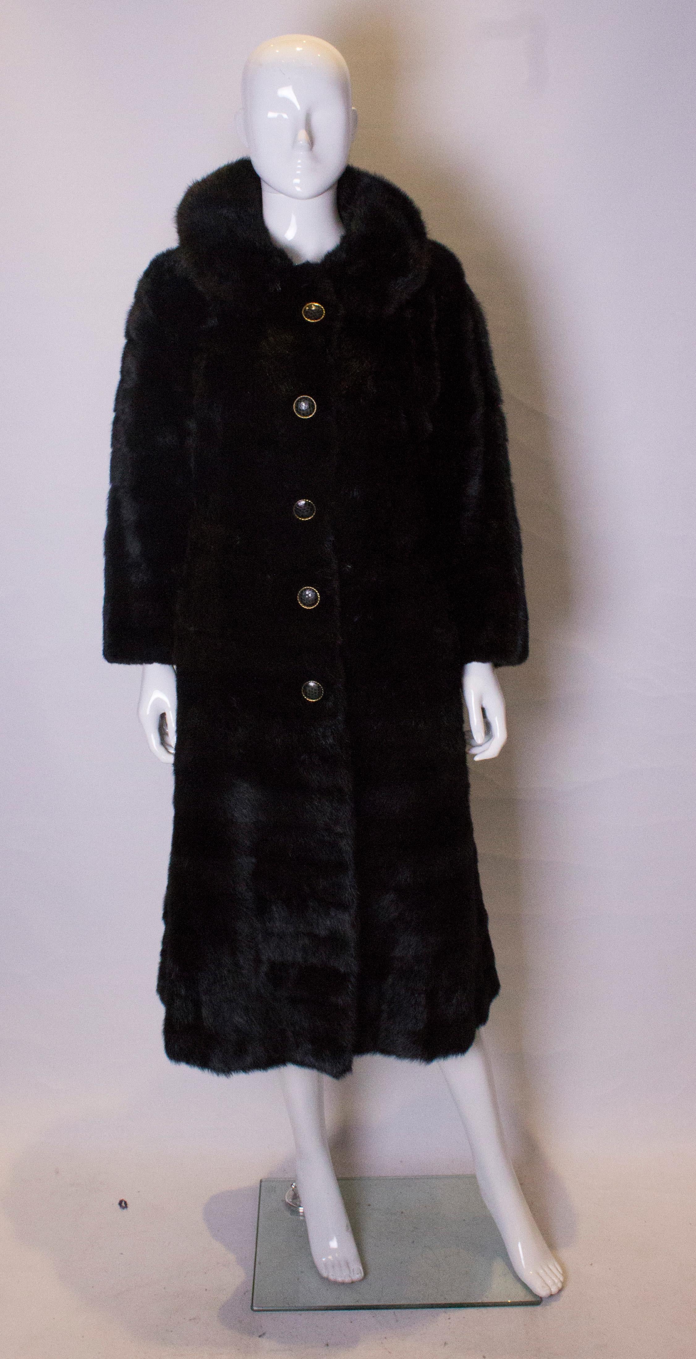 A chic dark mink coat, dating from the 1960s. The coat has a round collar , a five button/hook front fastening, two pockets at the front, and a half belt at the back. It is fully lined.