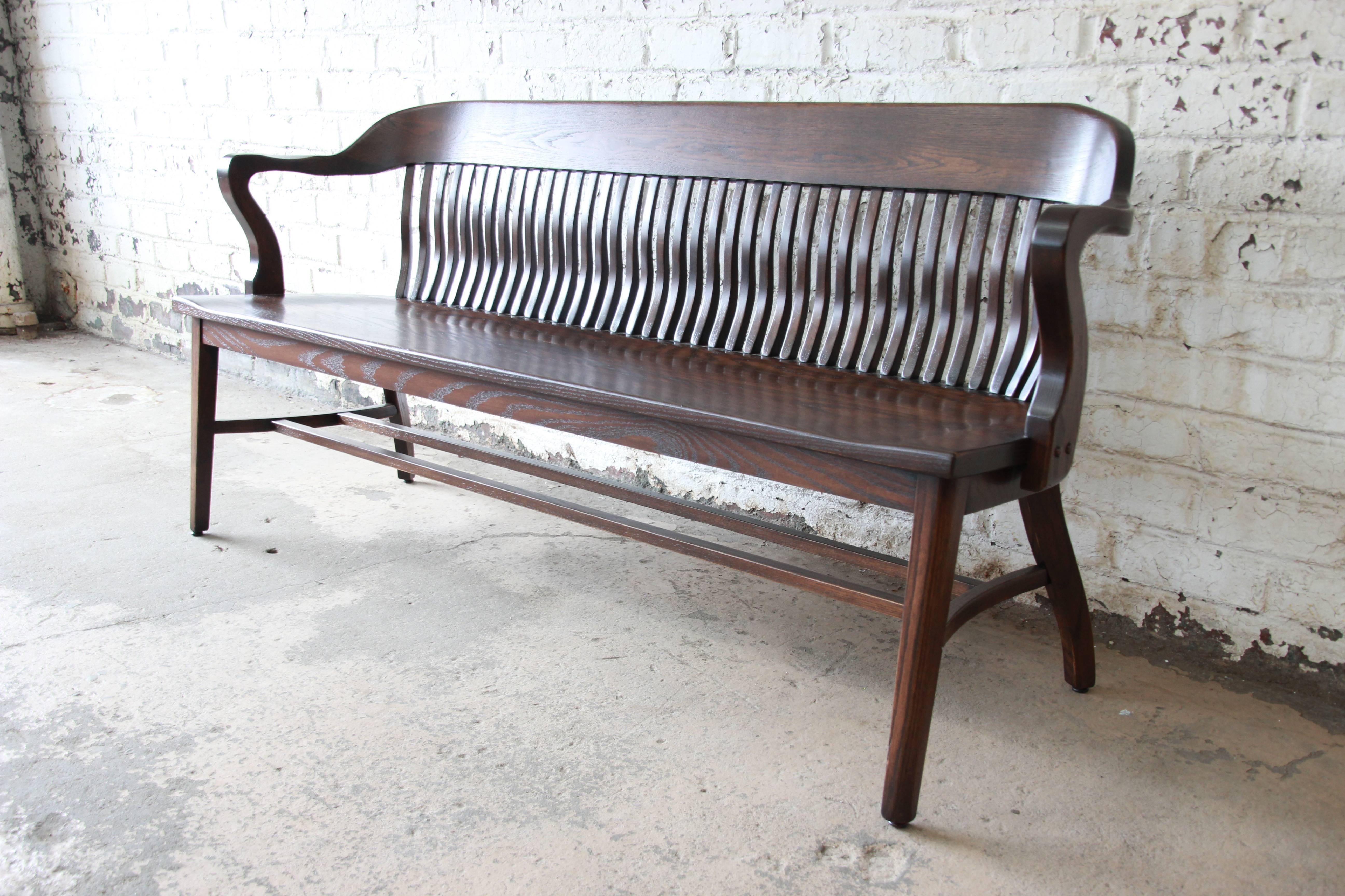An exceptional newly refinished lawyer's bench in solid oak. The bench has beautiful wood grain and is constructed with quality craftsmanship and detail. The curved back with spindles and armrest provide great comfort on this versatile piece. The