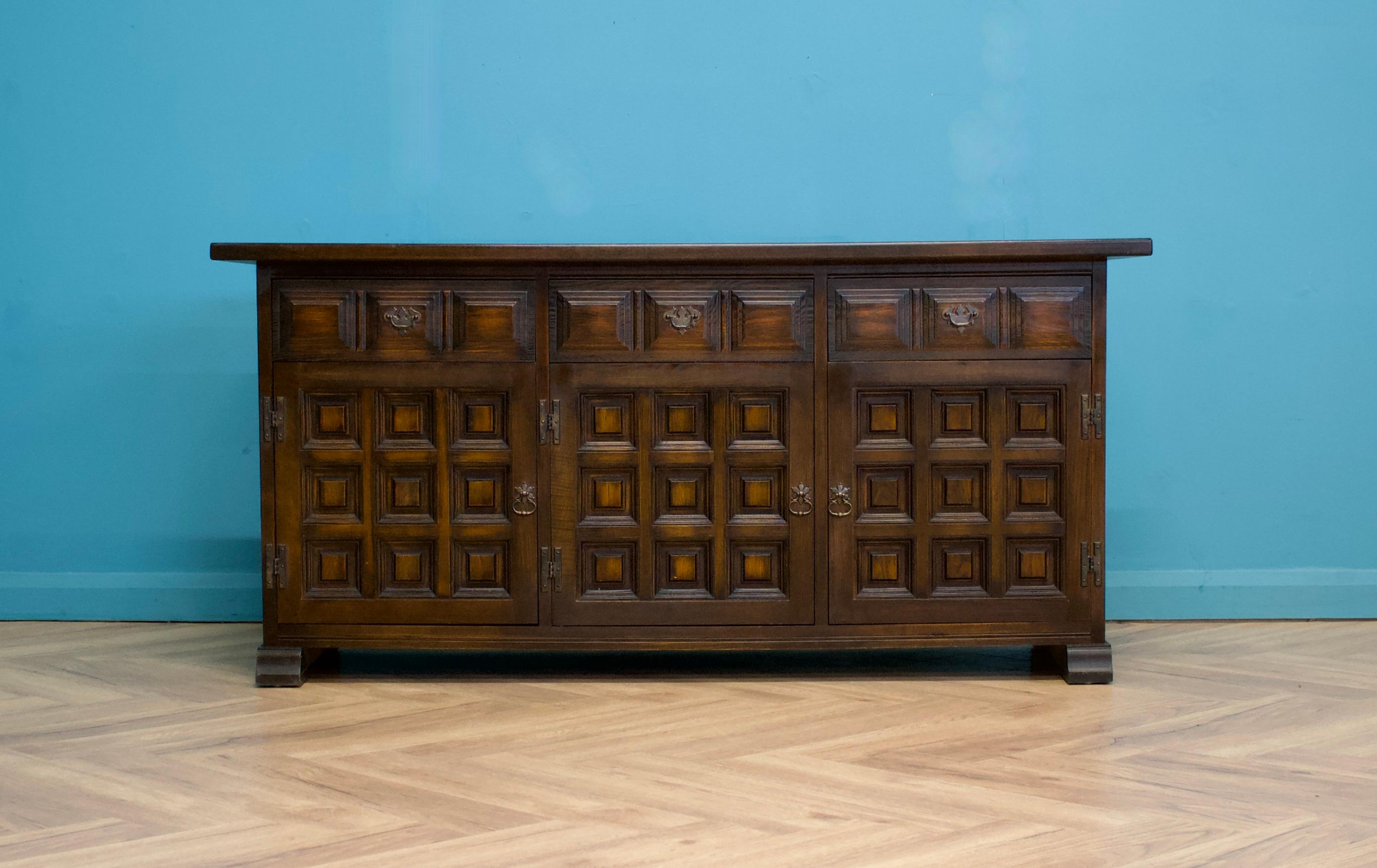 A beautiful quality Spanish influenced dark oak sideboard from the Toledo range, by Younger circa 1970s-1980s

There are two cupboards with shelves and three drawers.

Featuring a beautiful grained solid oak top.