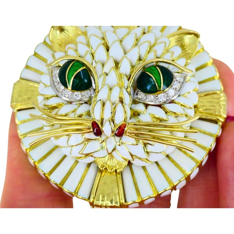 An impressive and fun David Webb cat brooch made of 18k gold, featuring enamel and diamond.
A striking feline face with a textured surface is brought to life with white enamel detailing that mimics fur. The deep green enamel eyes are framed by a