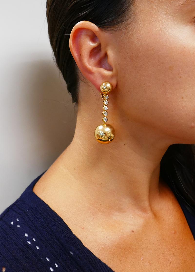 Ein Paar Ohrringe aus Gelbgold mit Diamanten von De Grisogono aus der Kollektion Boule.
Diese Vintage-Ohrringe bestehen aus einer größeren und einer kleineren Goldkugel. Die Kugeln sind durch einen Strang aus fünf Diamanten verbunden. Die Steine