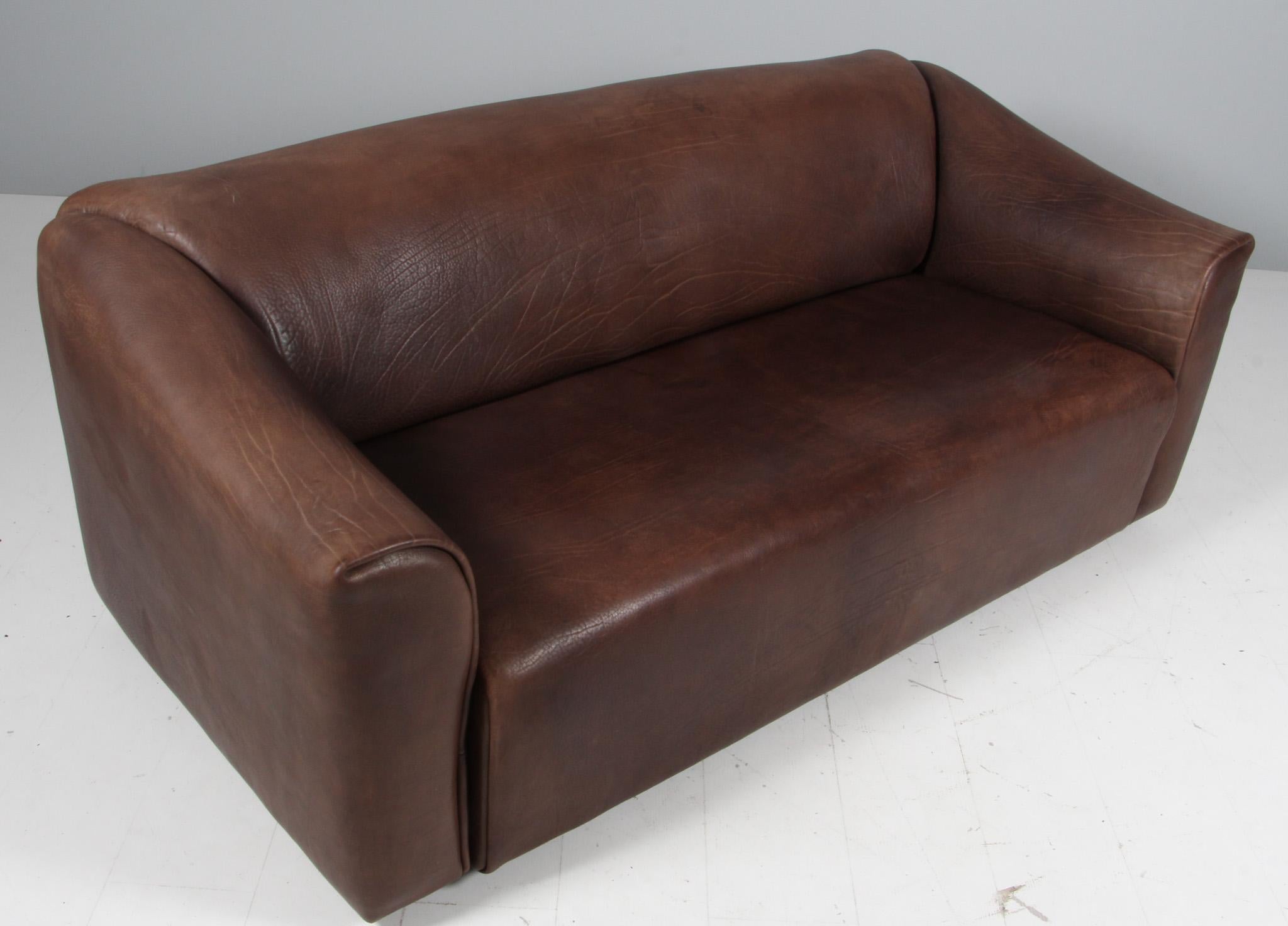 Confortable sofá DS47 de piel patinada de De Sede. El diseño es simplista, pero muy moderno. Un exterior apretado y cúbico con un interior suave y curvado, que acentúan el carácter confortable de este conjunto. La gruesa piel se coloca de una sola