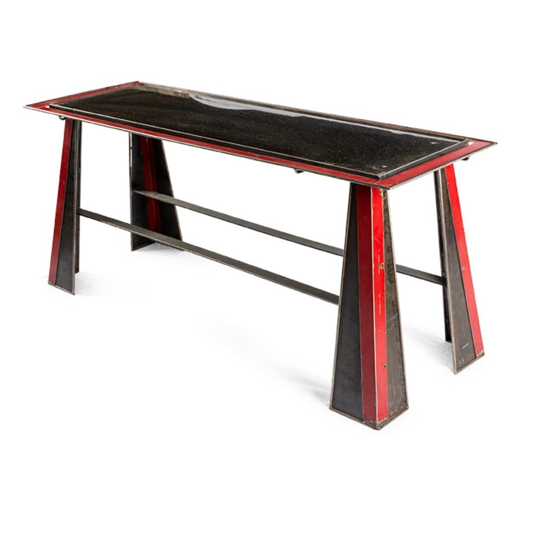 Esta consola metálica vintage combina influencias Art Déco con encanto industrial. El marco lineal se acentúa con detalles pintados en rojo y negro, con una pátina naturalmente envejecida y auténticos desgastes que añaden carácter y profundidad. Su