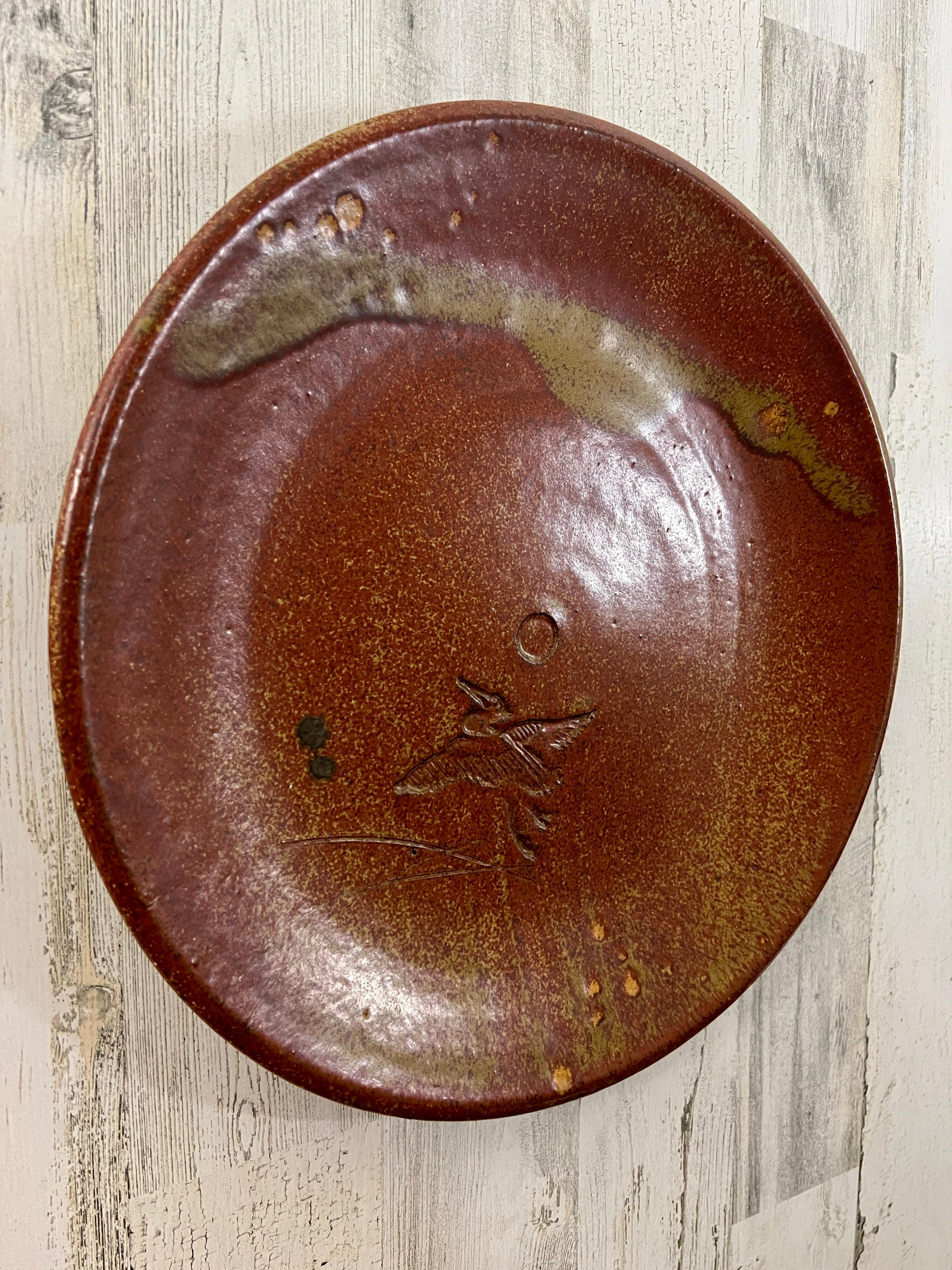 Ceramic charger with bird and sun design embossed into lower front of the plate. Signed and stamped on the backside.